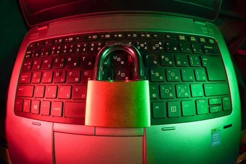 A laptop keyboard with a safety padlock placed in the center, illuminated by red and green lighting.