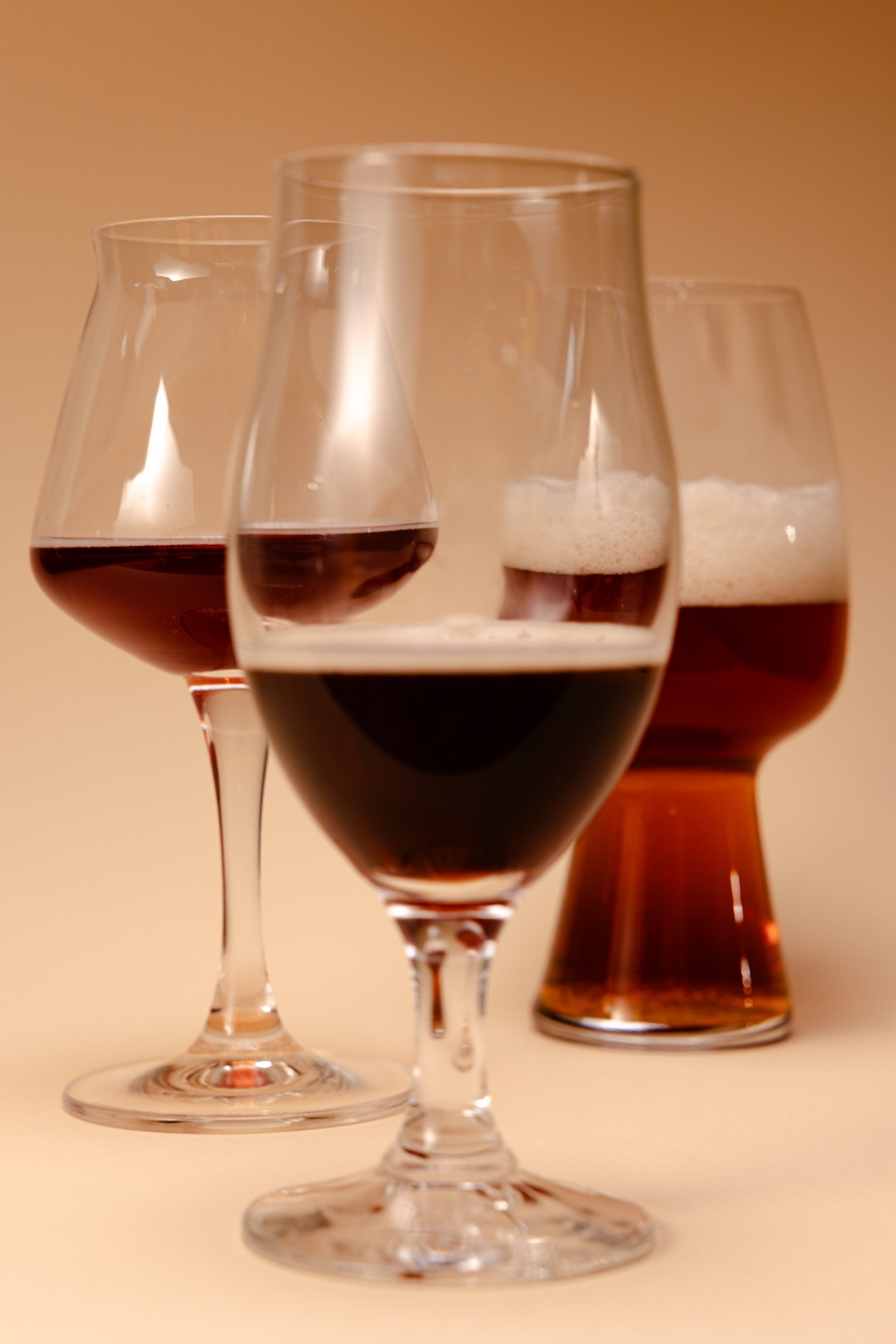 Mehrere Biergläser mit verschiedenen Biersorten vor einem beige Farbhintergrund.