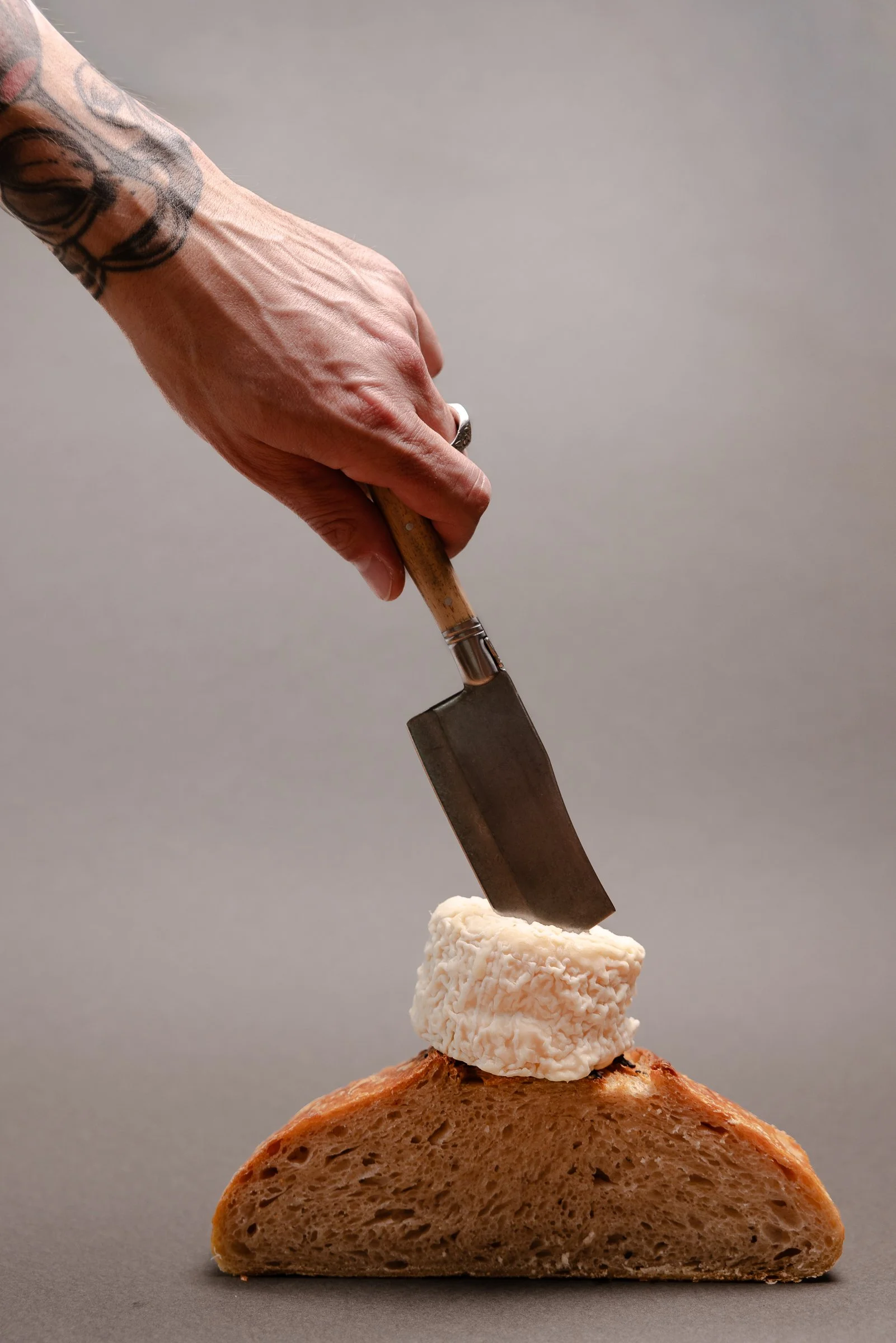 Ein Stück knuspriges Brot, darüber ein stück Weichkäse ein Hand, die mit einem Messer den Käse schneidet.
