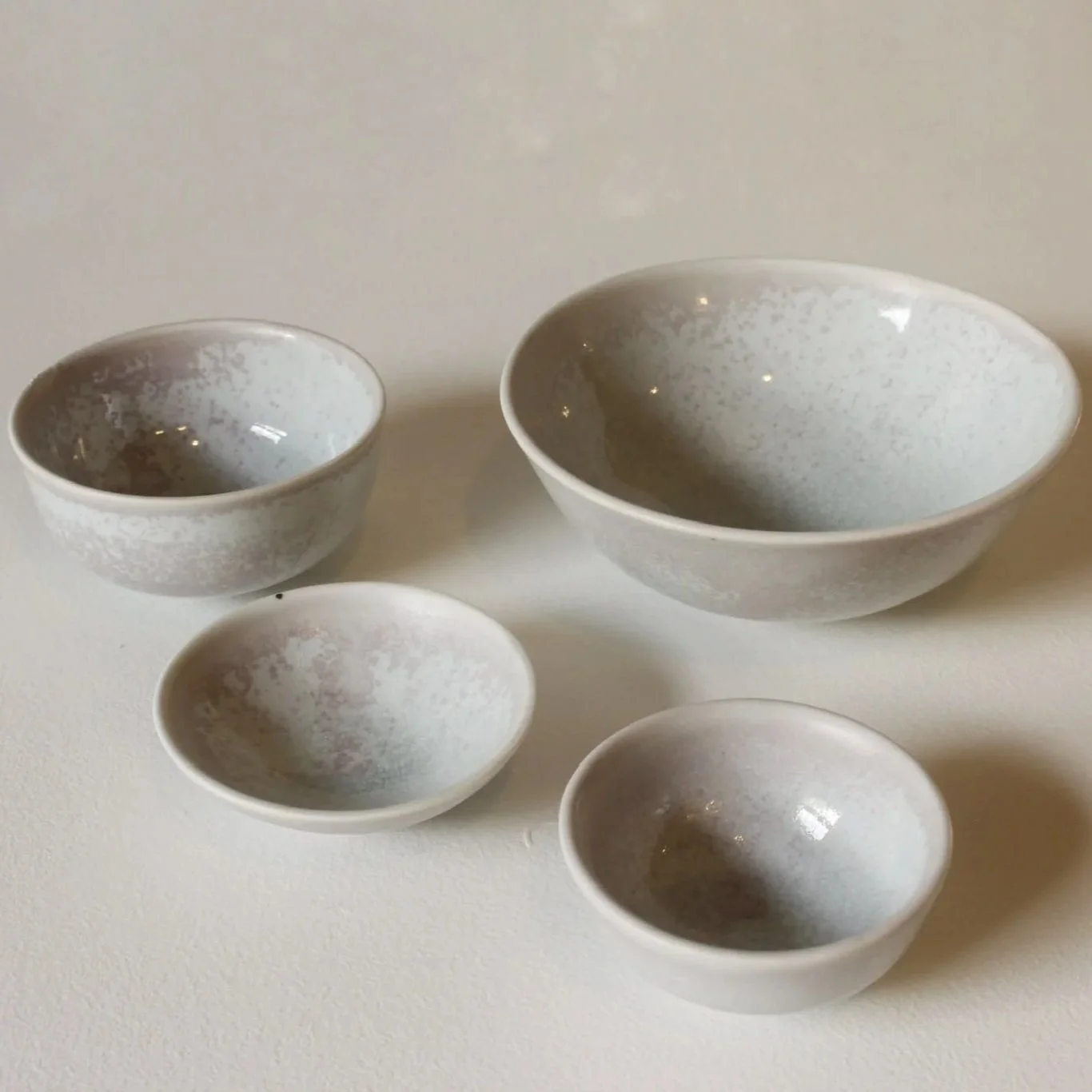 Set of five white ceramic bowls with a subtle speckled pattern, varying in size, arranged on a white surface.