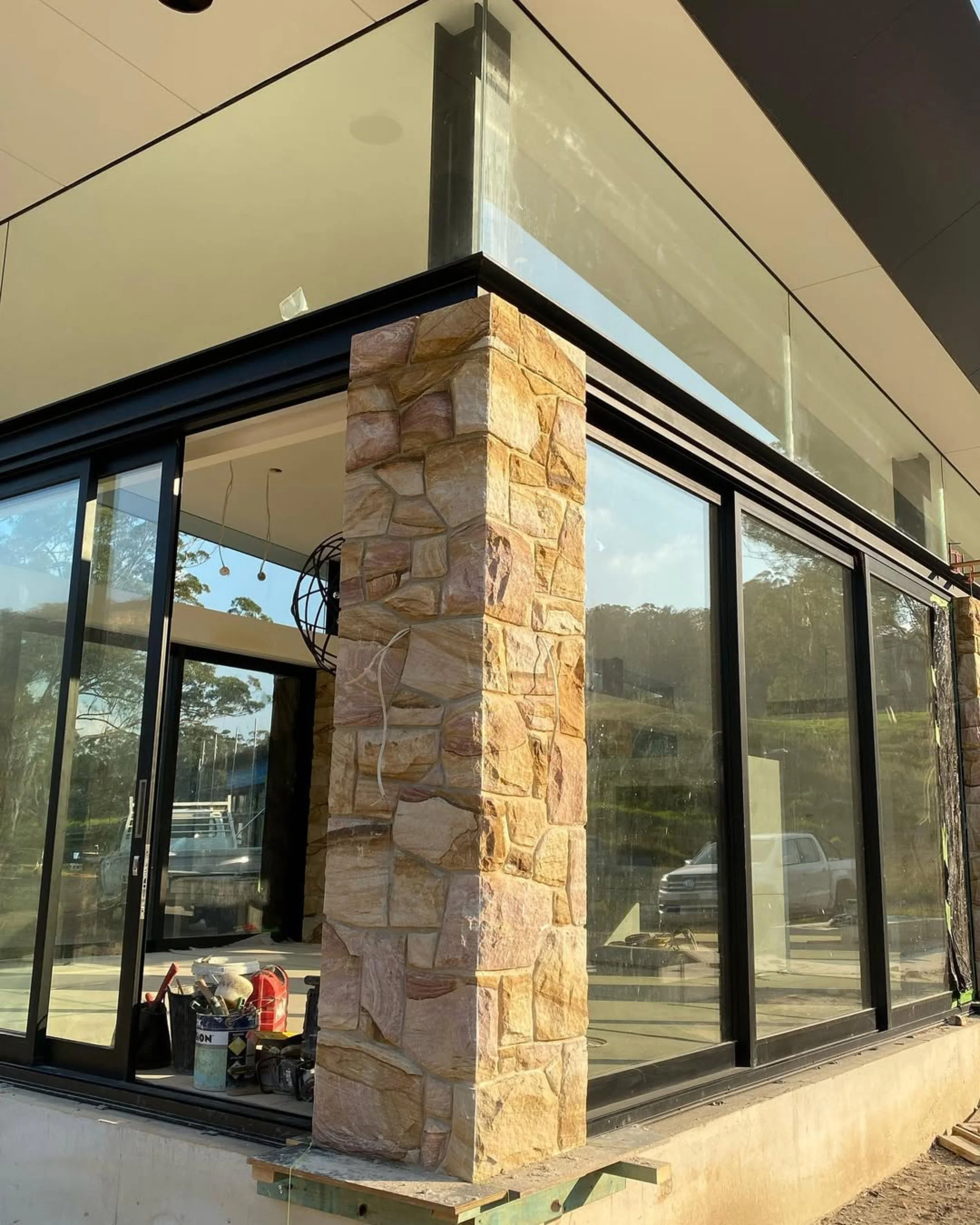 Building under construction with stone pillar and glass walls, construction tools and materials on the ground.