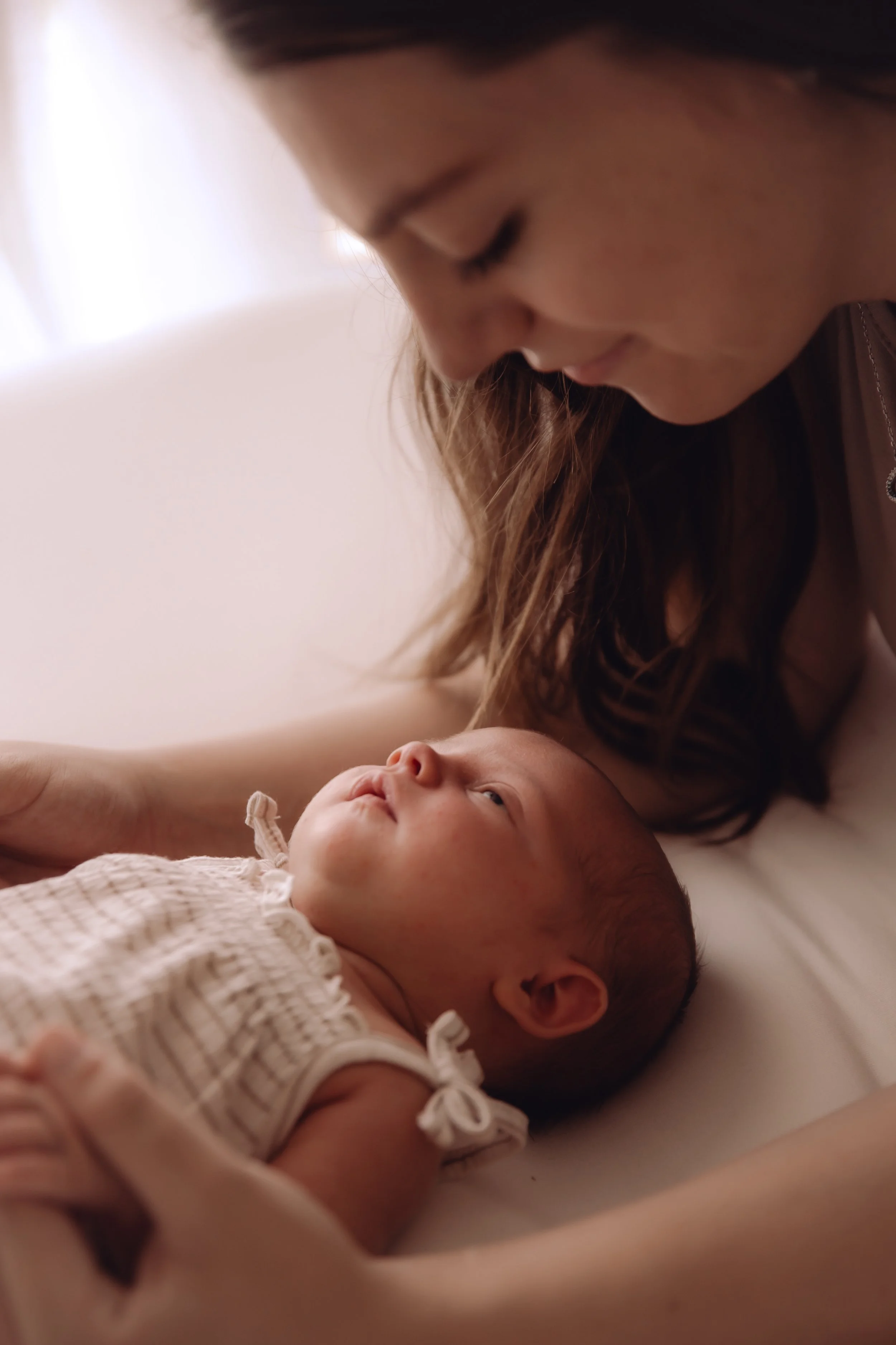 A woman looking down at a baby lying on a bed.