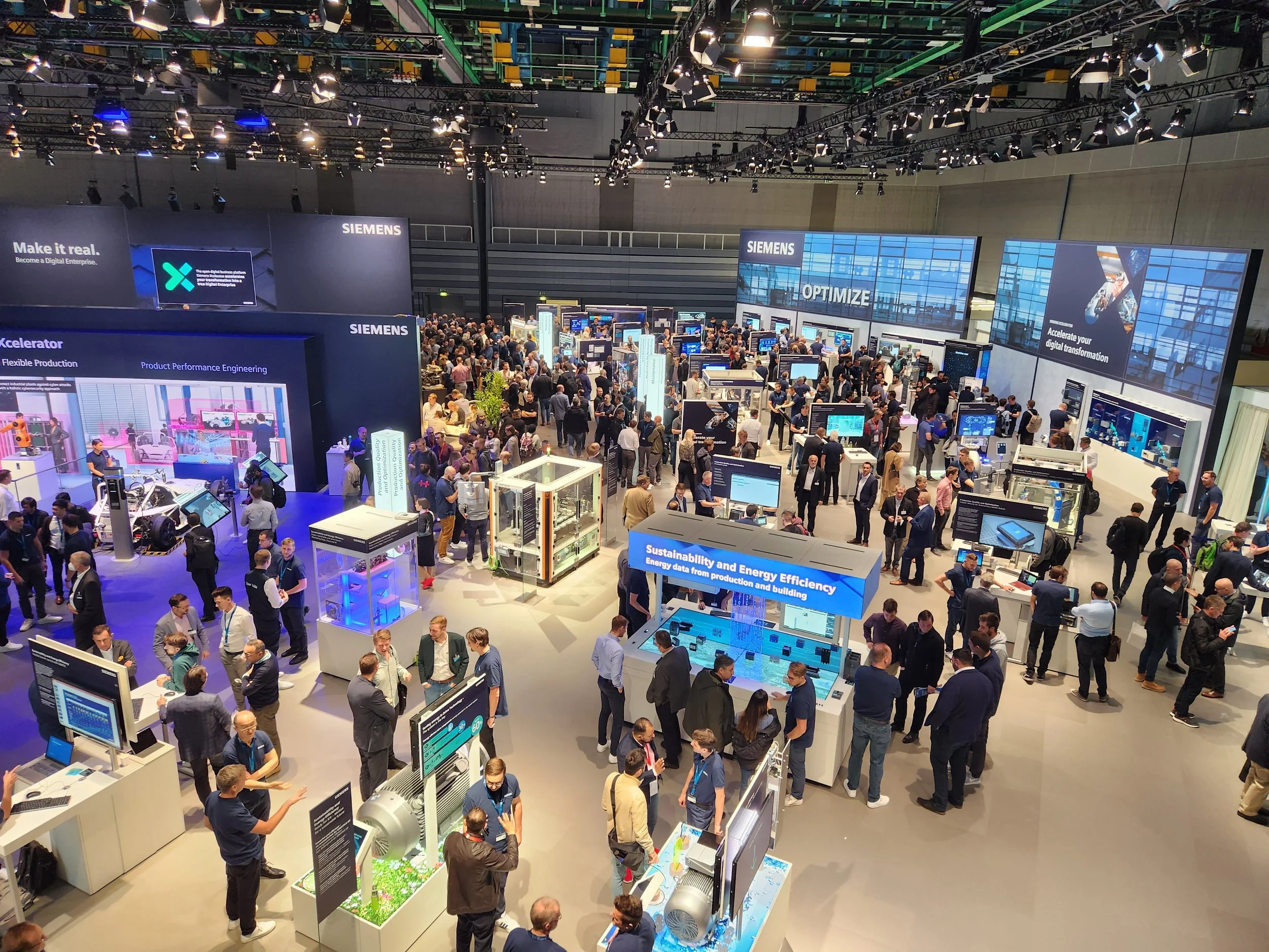 A crowded SPS Messe Nuremberg exhibition hall with multiple booths, monitors, and displays showcasing Siemens products and solutions for digital transformation, energy efficiency, and industrial manufacturing.