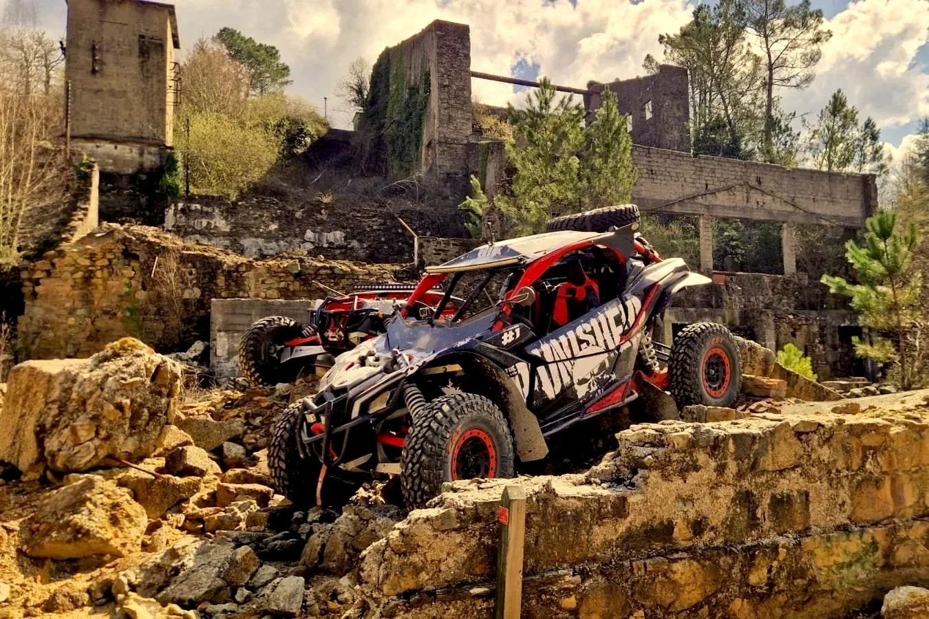 Veículo off-road Can-Am Maverick X3 em terreno rochoso do Norte de Portugal com construções antigas ao fundo.