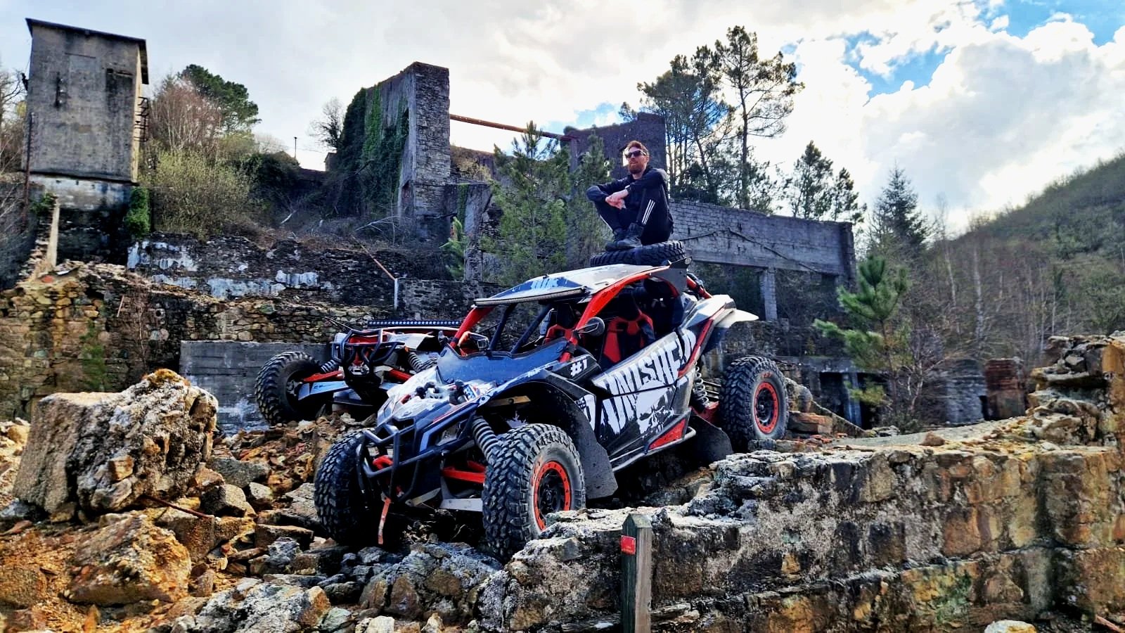 Homem sentado em um veículo de off-road em um ambiente de natureza com ruínas ao fundo.