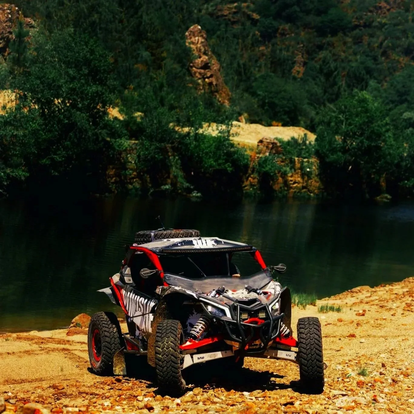 Veículo off-road estacionado à beira de um rio em um ambiente natural com árvores e rochas.