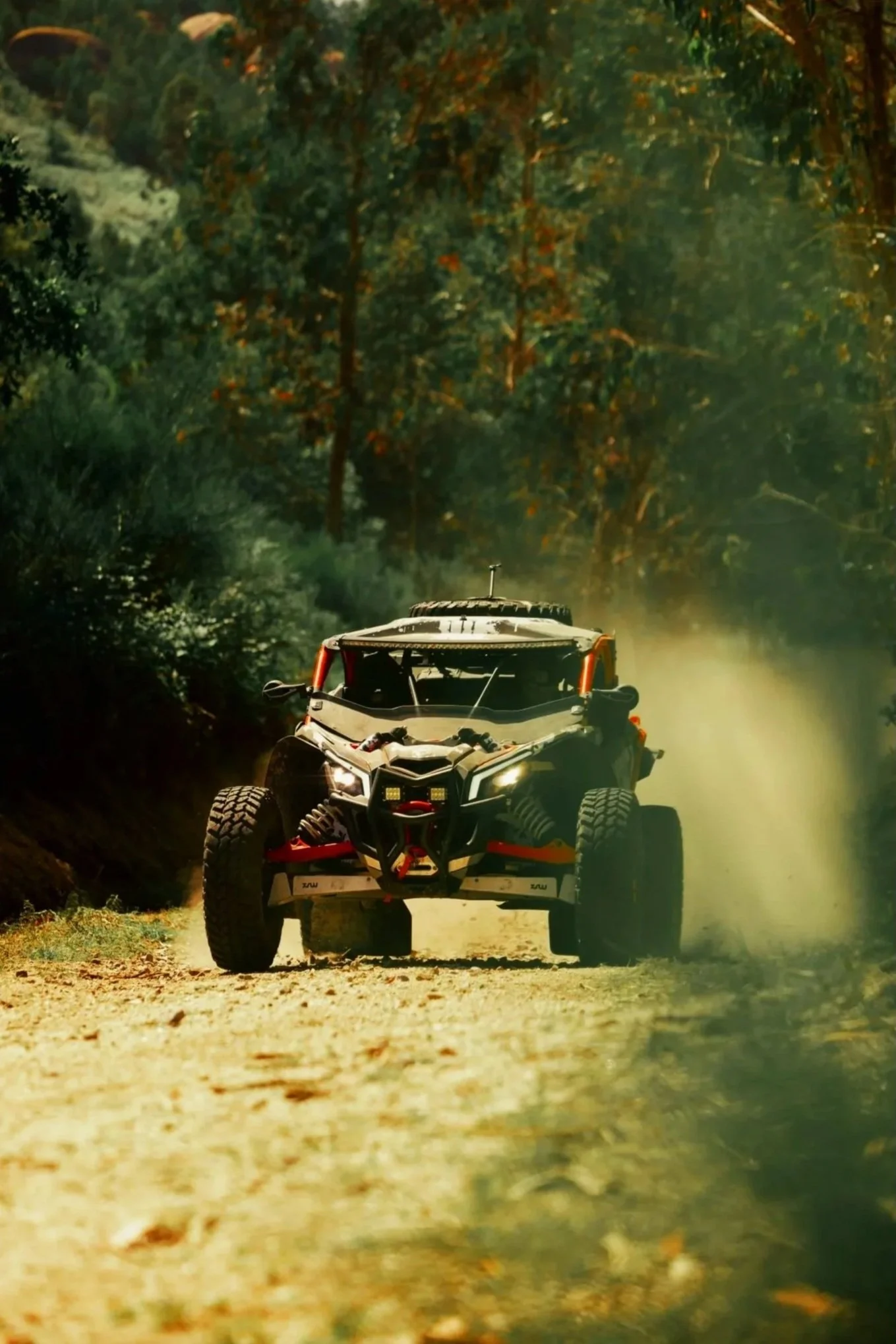 Veículo de off-road em um caminho de terra, rodeado por árvores com folhas verdes e um pouco de poeira levantada pela movimentação do veículo.