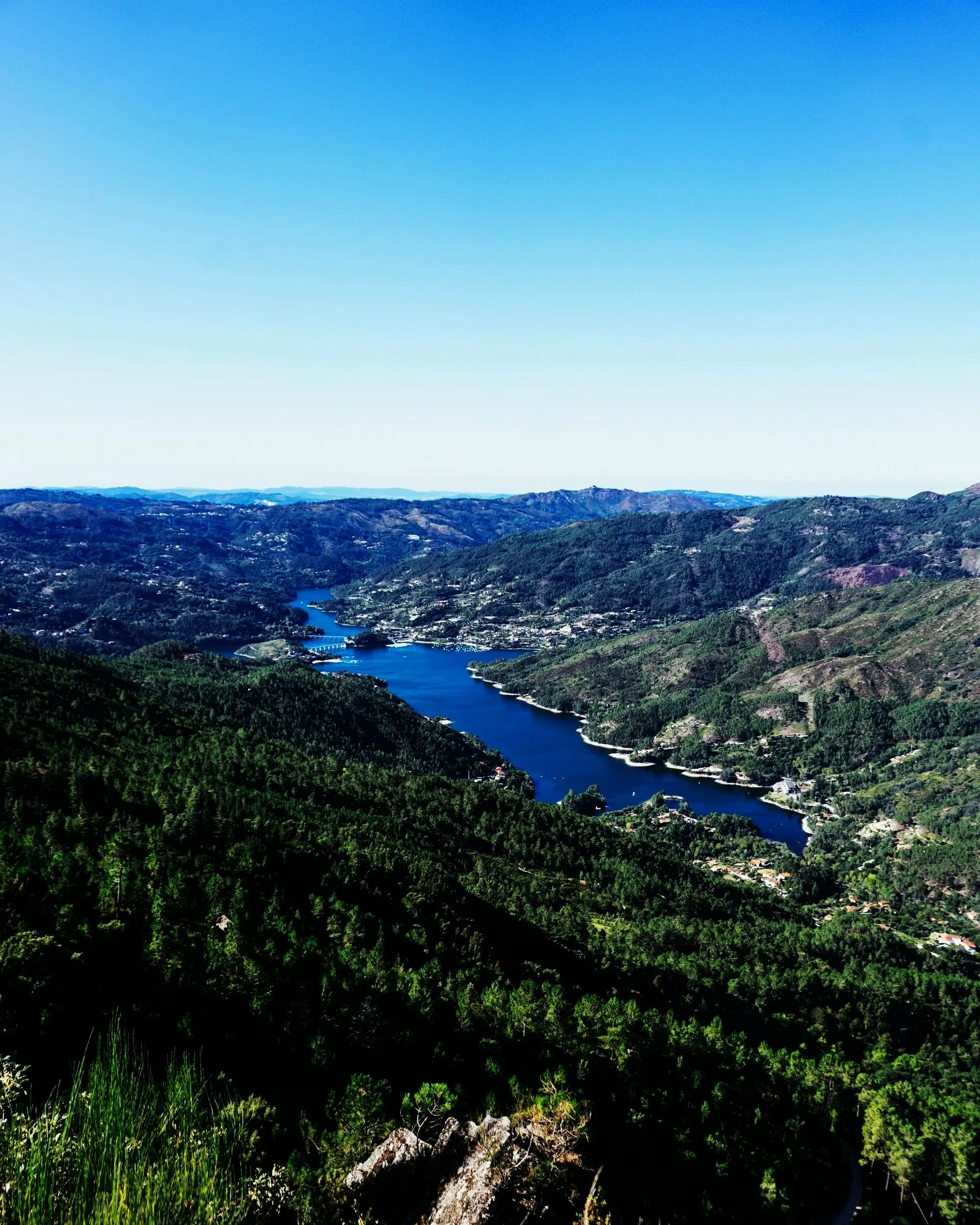 Paisagem de horizonte com rio serpenteando por entre montanhas verdes sob céu claro.