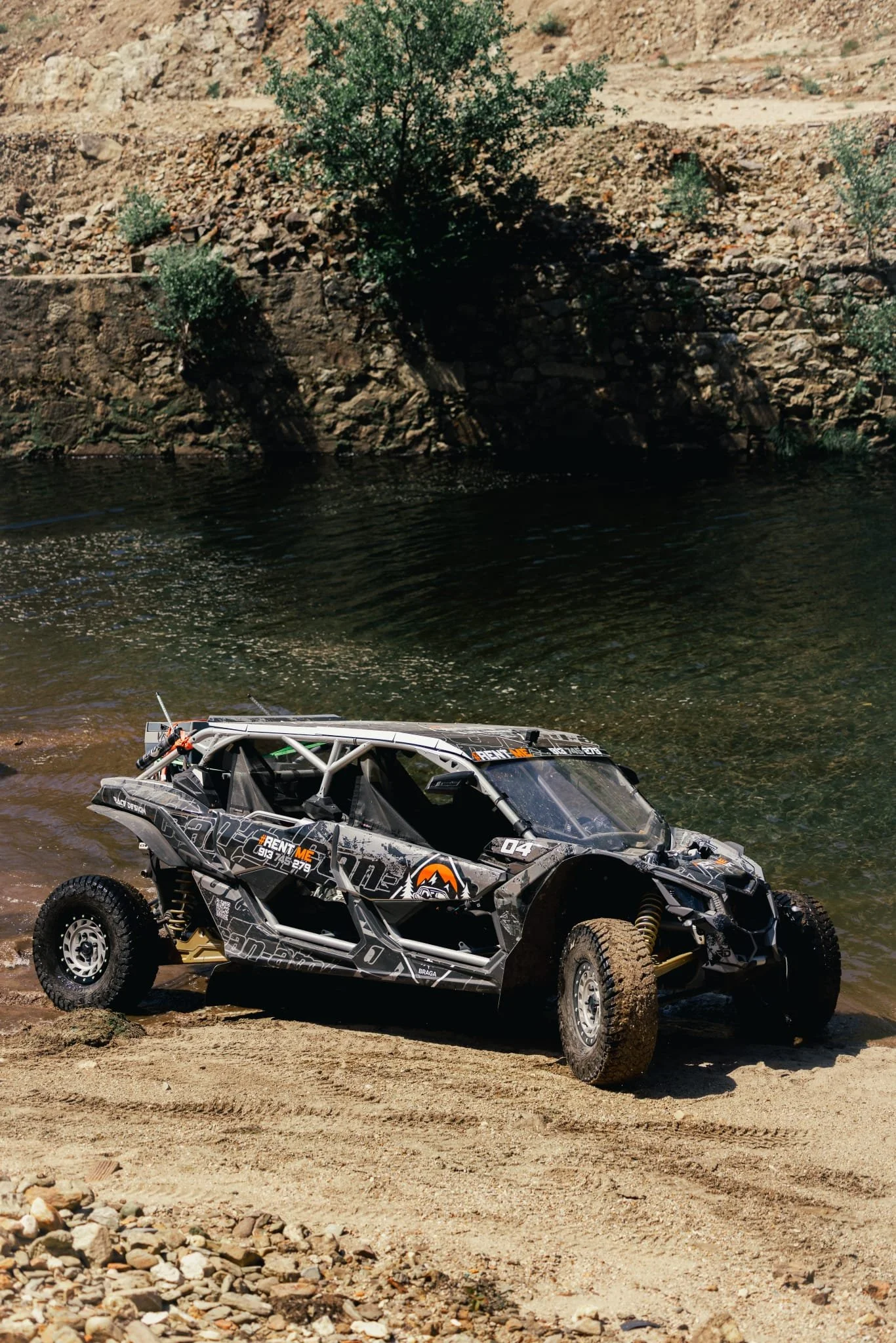 Veículo off-road em trilha arenosa ao lado de um rio com vegetação ao fundo.