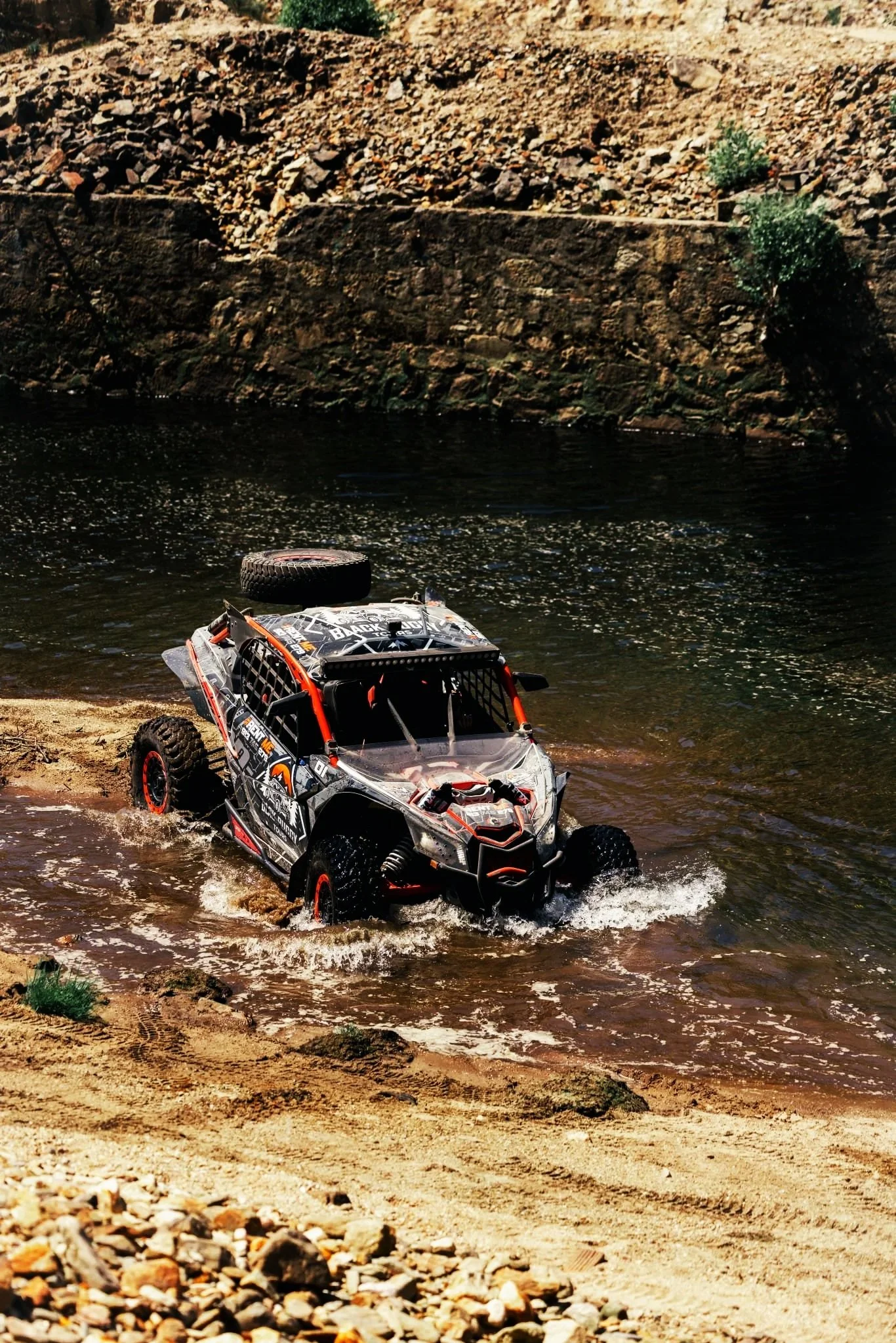 Buggy Can-Am Maverick X3 a atravessar rio no Gerês,  ao lado de margem de areia e rochas, em tour off-road de aventura na região de Braga - Black Buggy Tours 