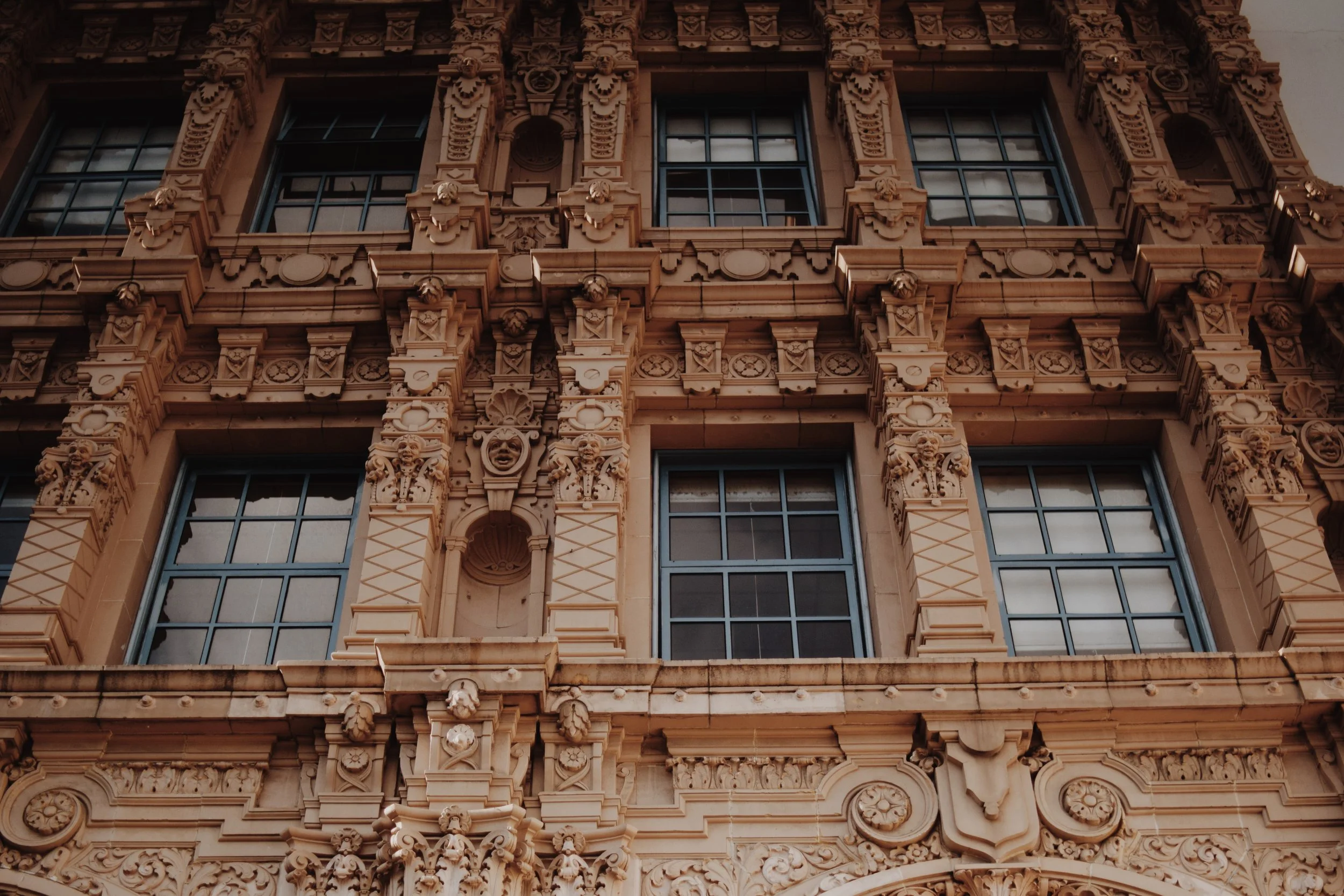 Close-up of a historic building's ornate stone facade with large windows, detailed carvings, and decorative sculptures.