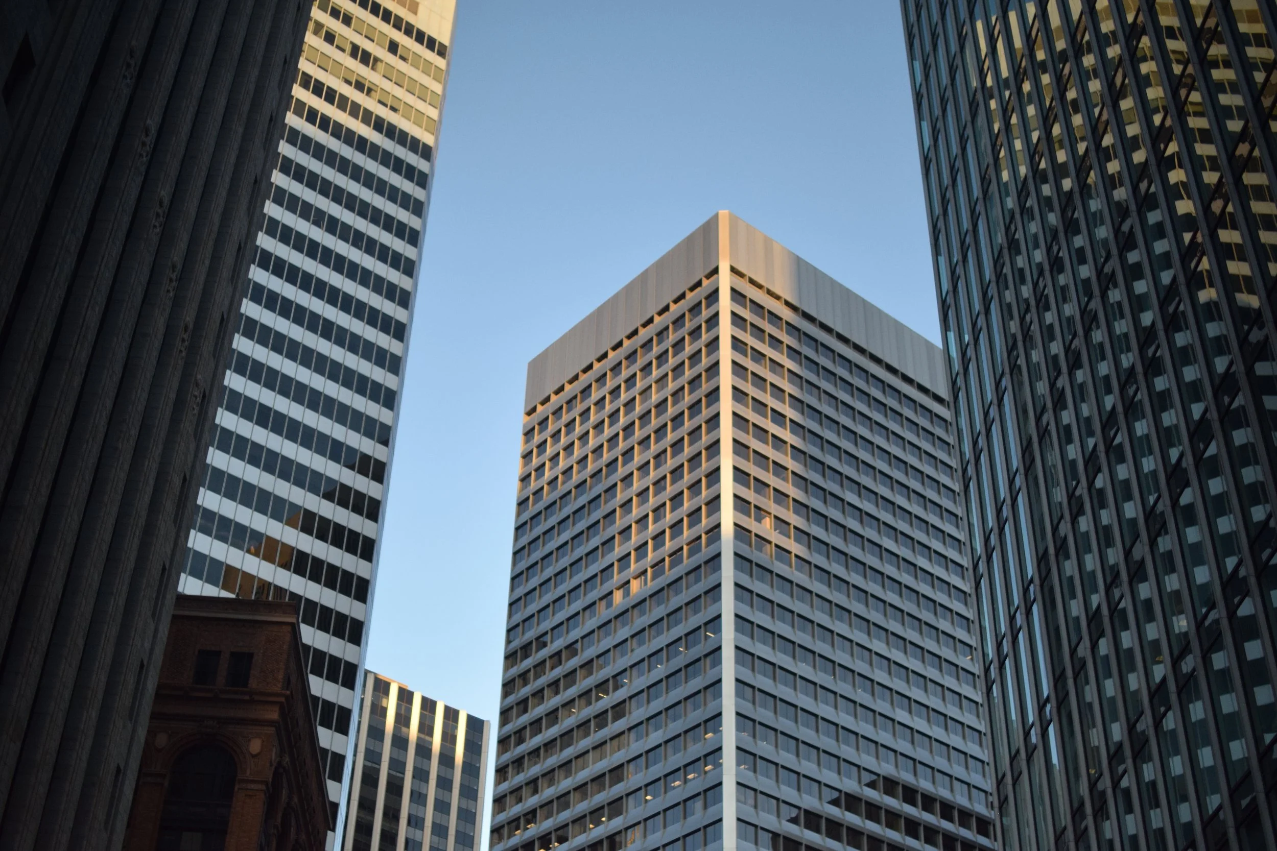 View of three tall skyscrapers from street level with clear blue sky in background.