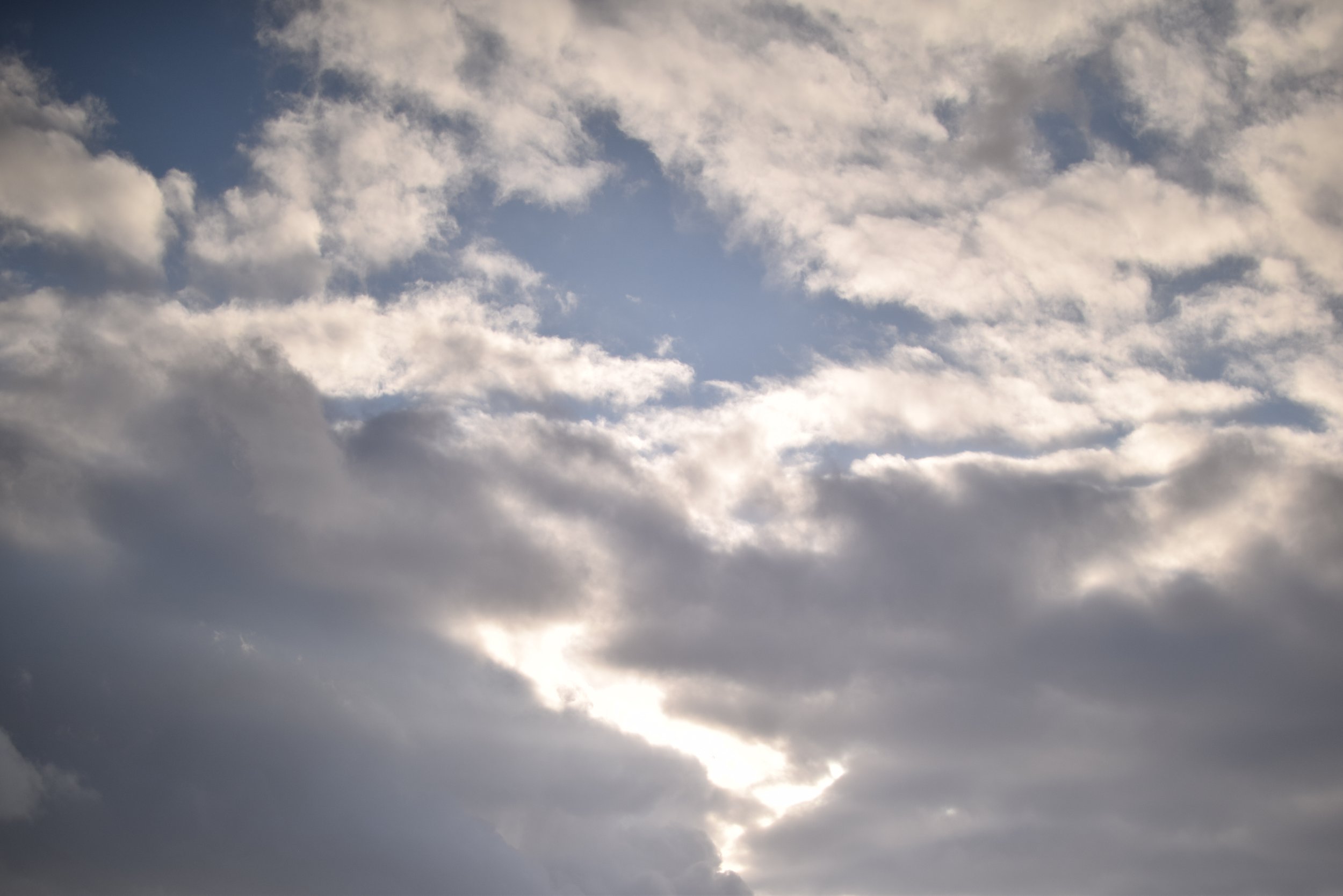 A partly cloudy sky with sunlight peeking through the clouds.