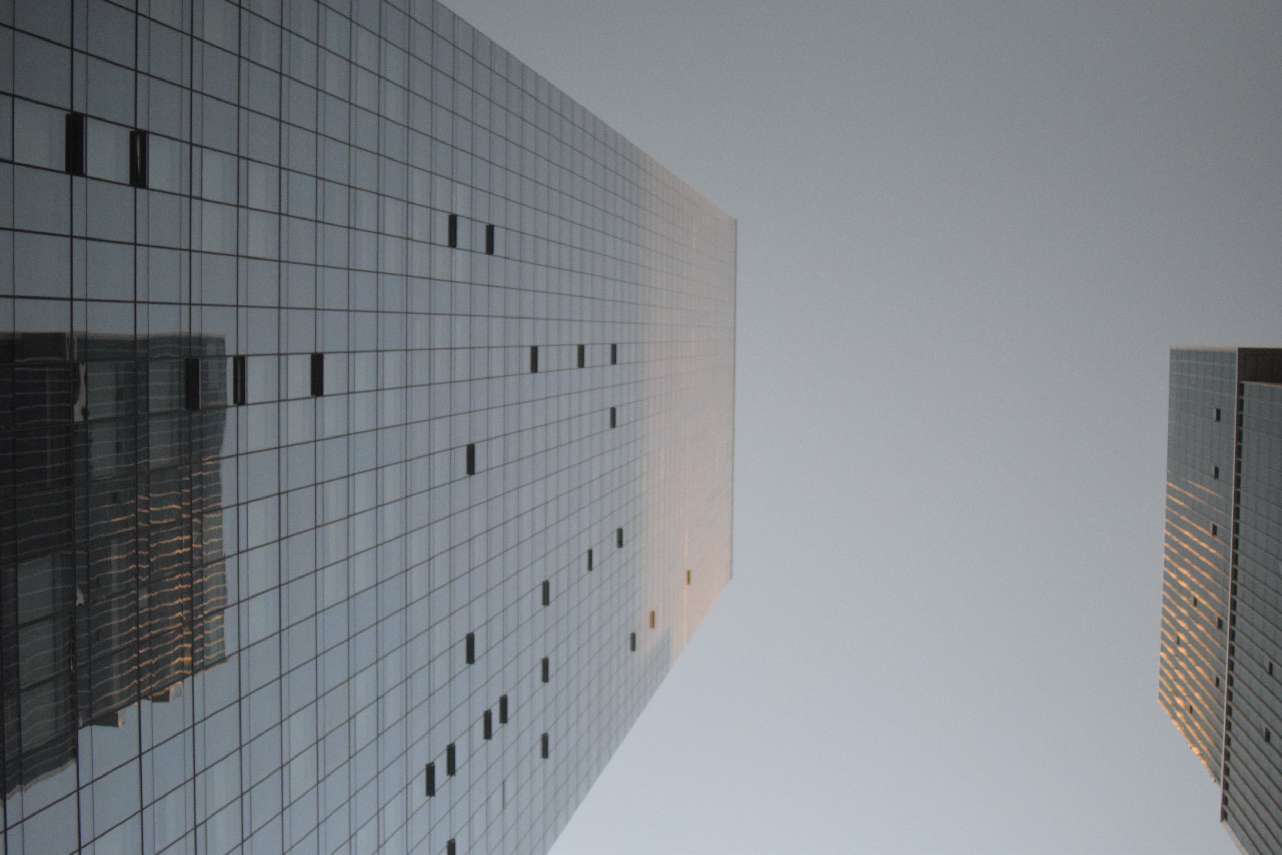 Tall modern glass office buildings reflecting the cloudy sky.