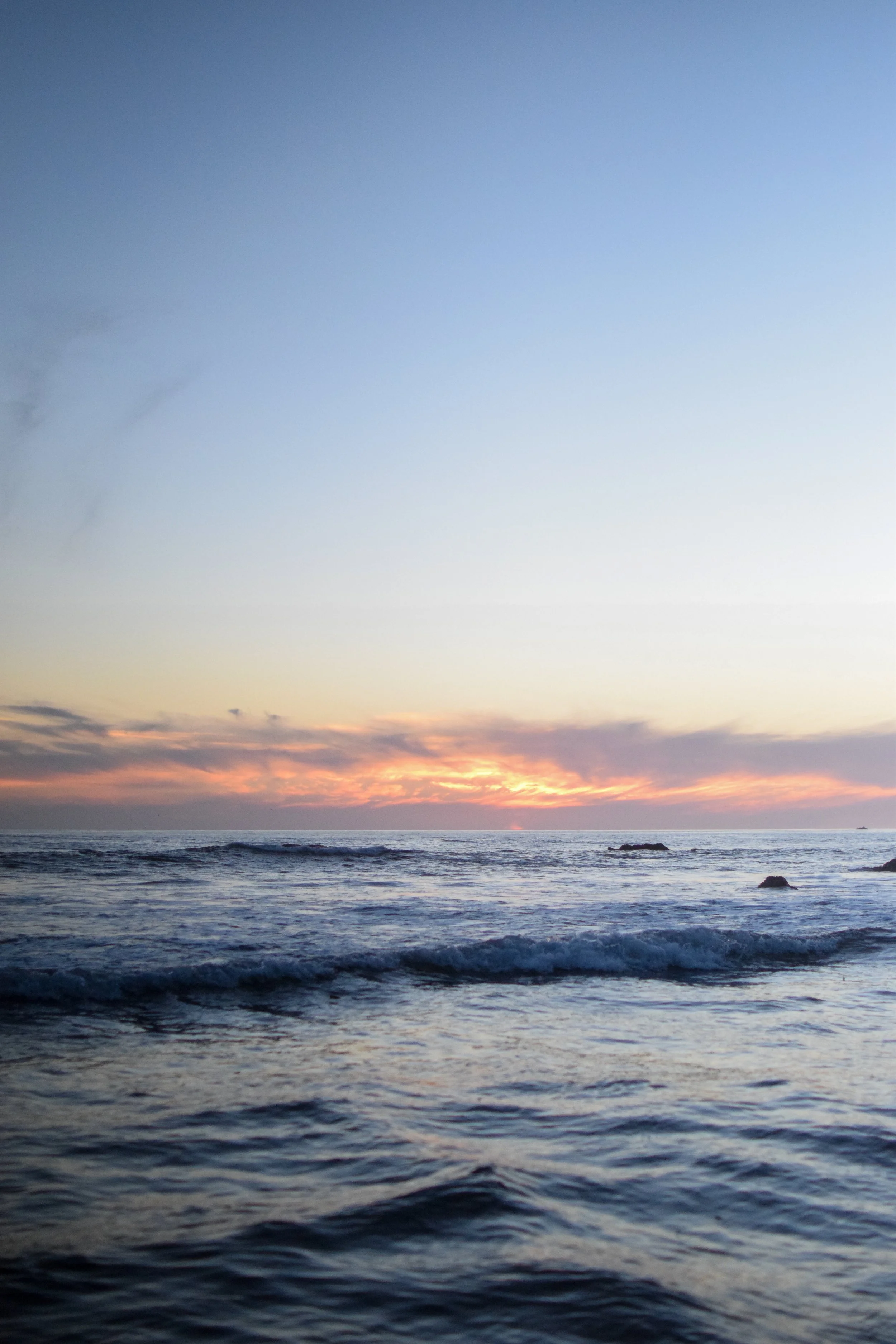 A photo of the ocean at sunset with waves and a colorful sky.