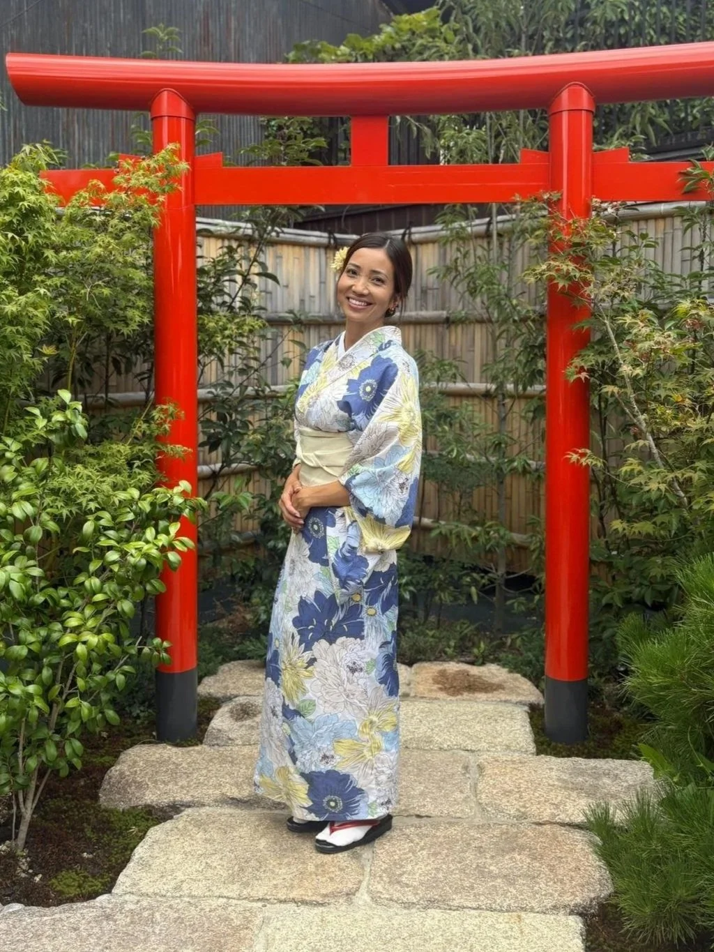 Jacque, guia brasileira radicada no Japão, vestindo quimono em jardim japonês com torii vermelho