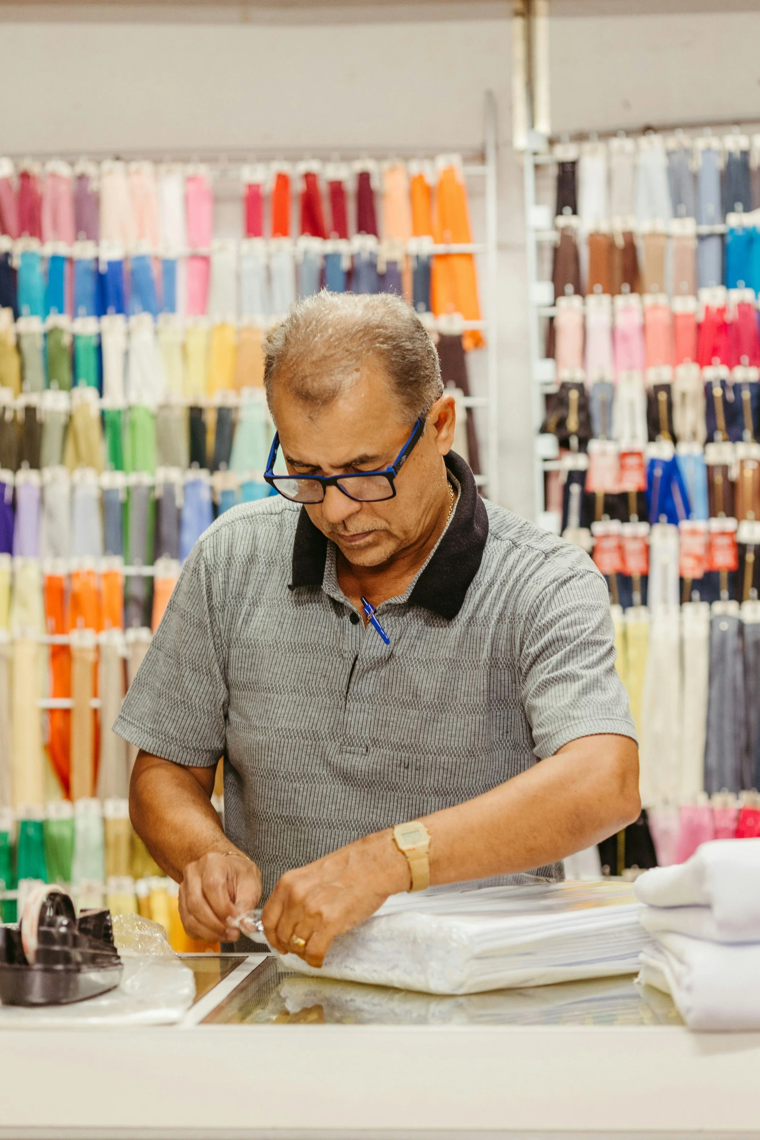 A man working with fabric at a store with colorful fabric rolls in the background.