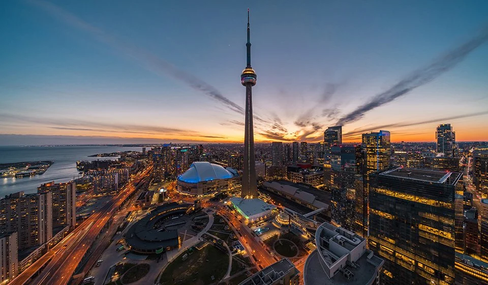 Aerial view of Toronto downtown at sunset, featuring the CN Tower, Rogers Centre stadium, and surrounding skyscrapers.