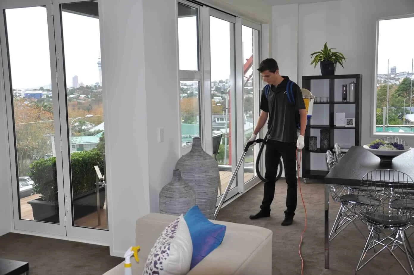 Man cleaning the floor in a modern living room with large windows and outdoor view.