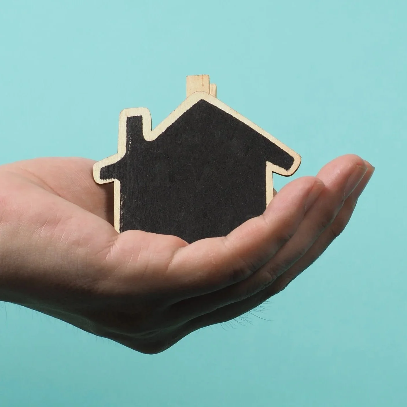Una mano tiene una figura de una casa de madera con la parte central pintada de negro, formando un símbolo llamado 'techo y pared'.