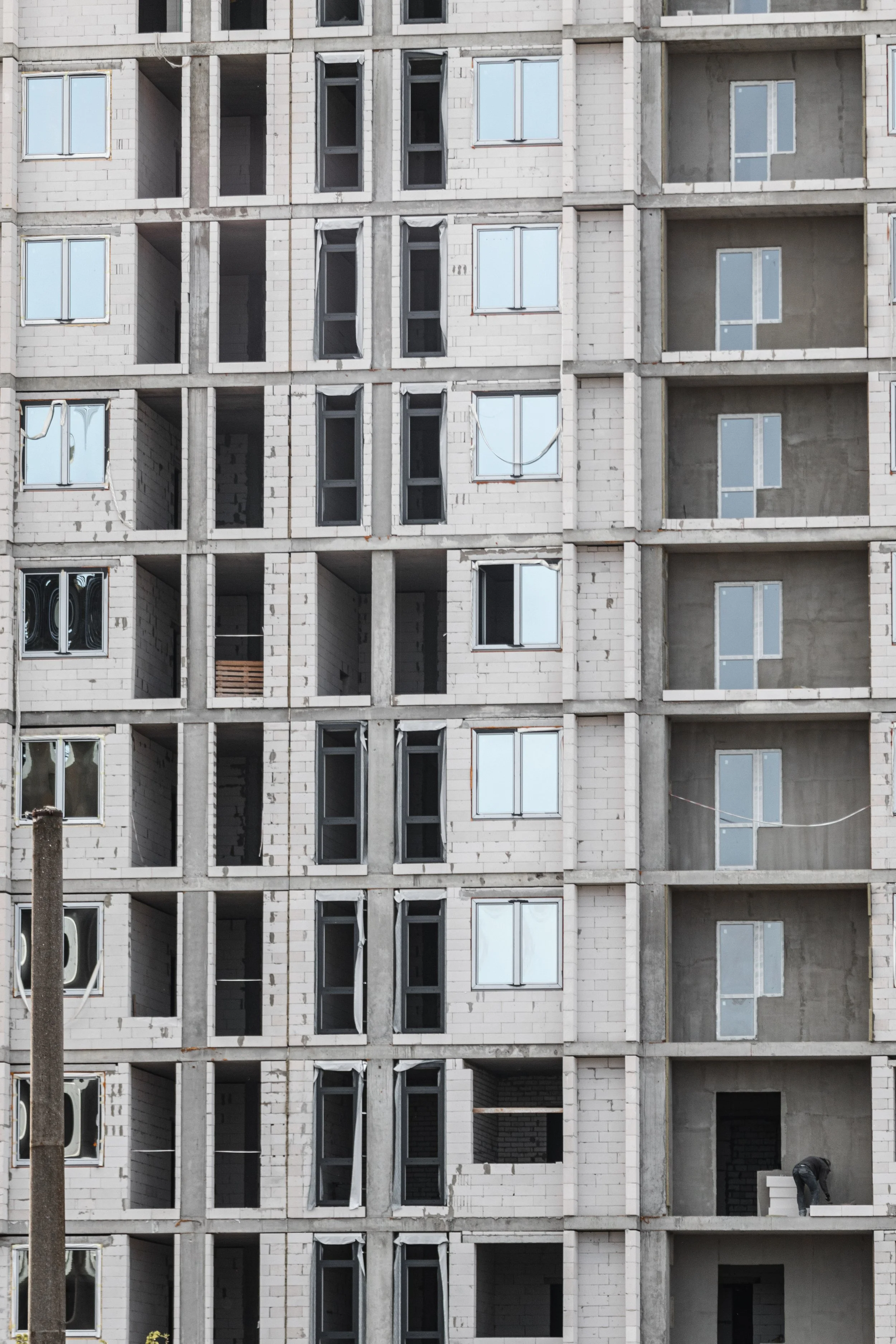 Cantiere edile di un edificio in costruzione con pareti in mattoni e finestre ancora da installare, alcune persone sul sito.
