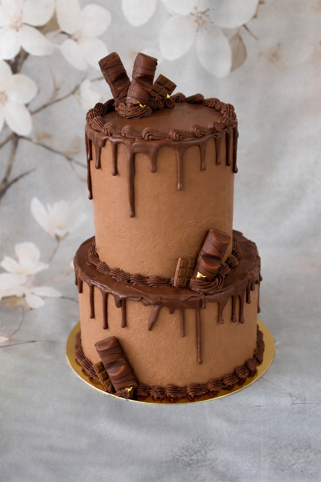 Gâteau chocolaté à deux niveaux avec un glaçage lisse et un décor de chocolat en forme de barres et de rubans, avec du chocolat qui coule sur les bords.