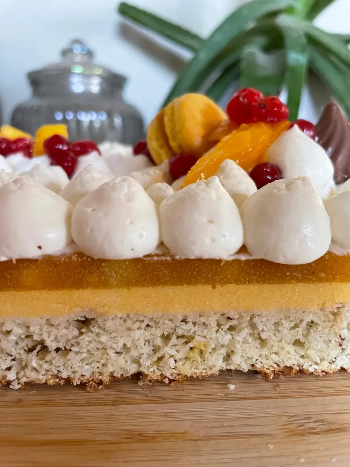 Gâteau à étages avec décor de fruits et crème, comprenant une base de gâteau blanc avec une couche de fruits colorés, y compris des fruits rouges, des morceaux d'orange et une décoration en macarons et petits choux.