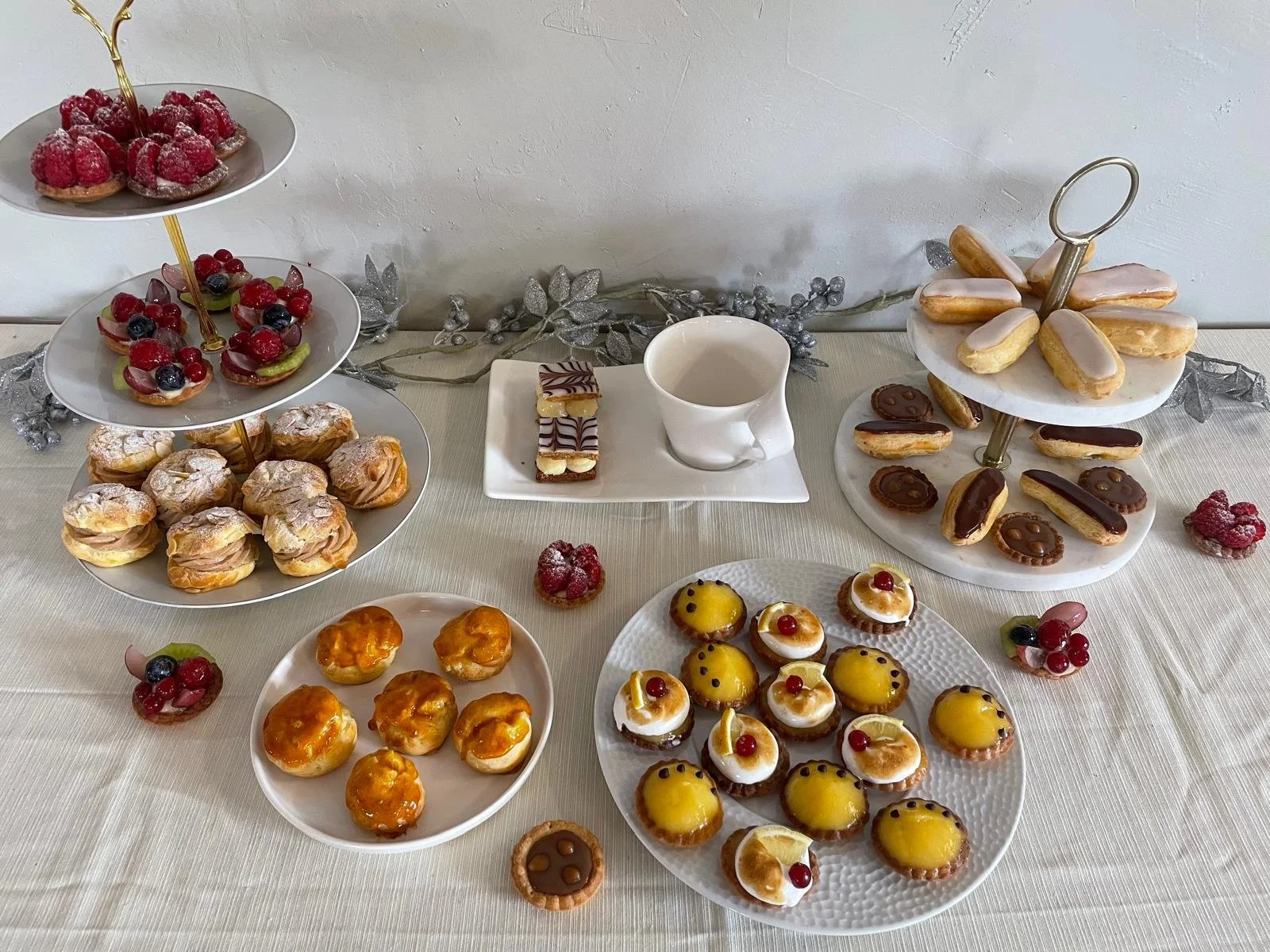 Un service de goûter avec diverses pâtisseries, notamment des tartes aux fruits, des éclairs, des mini tartelettes, des biscuits à la crème, et un assortiment de biscuits à la couche blanche et chocolat, présenté sur deux plateaux tournants, avec quelques petits desserts individuels sur la table.