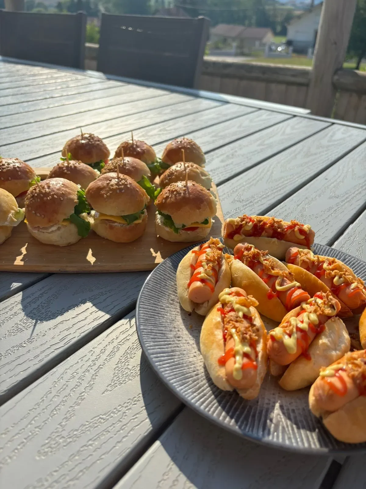 Mini sandwich et hot dogs sur une table en bois, avec un fond extérieur en plein soleil.