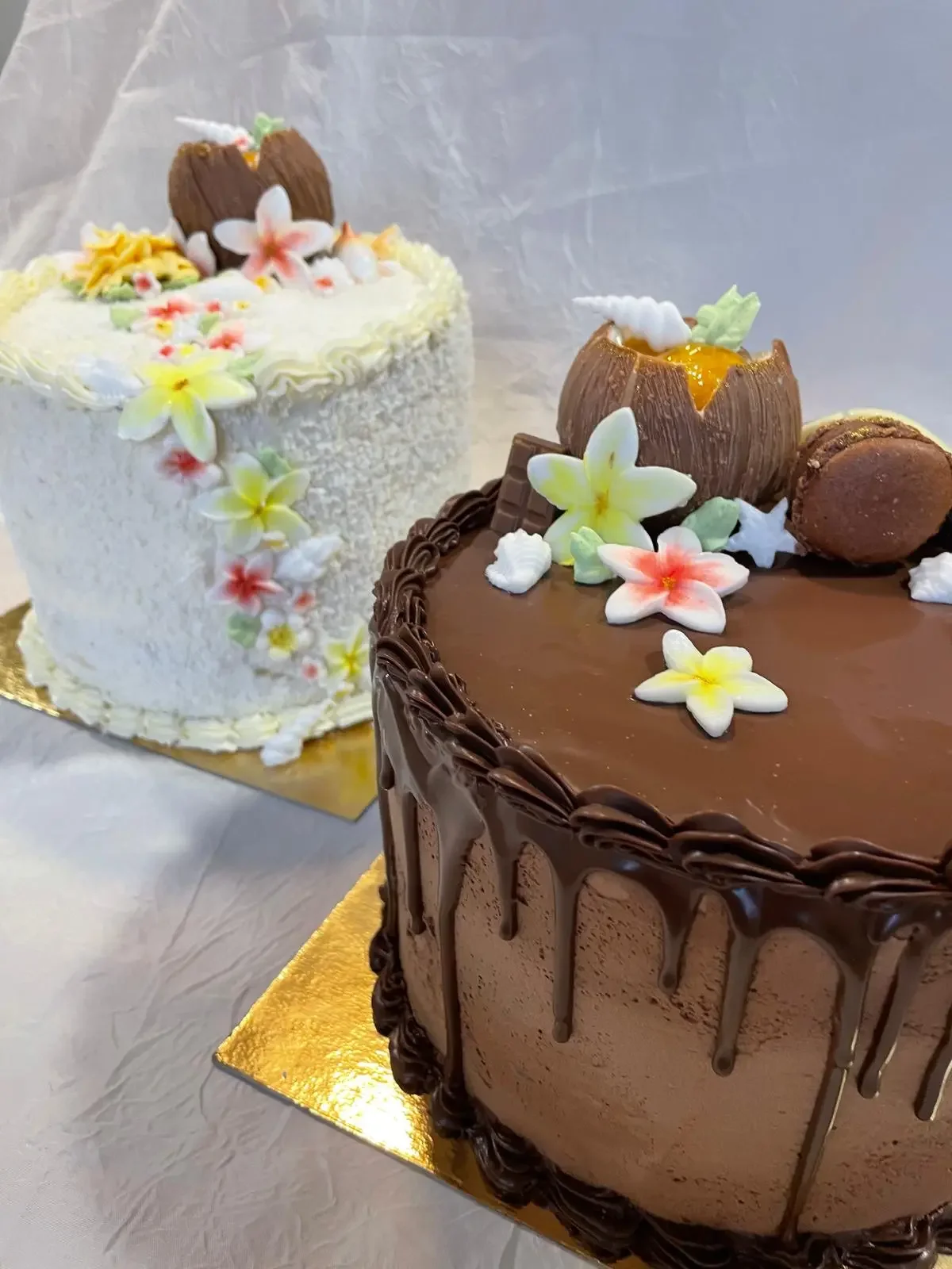 Deux.gâteaux d'anniversaire décorés avec des fleurs en pâte à sucre, un gâteau au chocolat avec une ganache chantilly et un autre à la crème blanche avec des fleurs et un petit cheval en pâte à sucre.