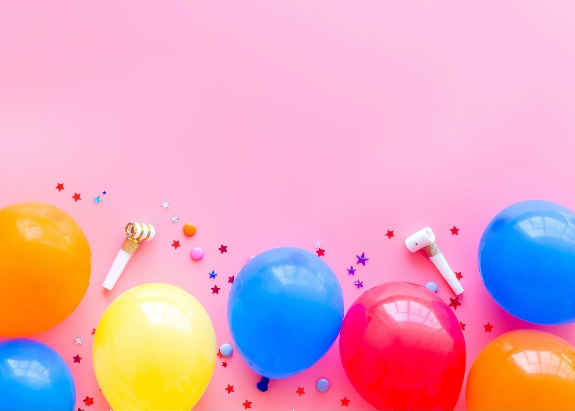 Colorful balloons, star-shaped confetti, and party blowers scattered on a pink background for a celebration.