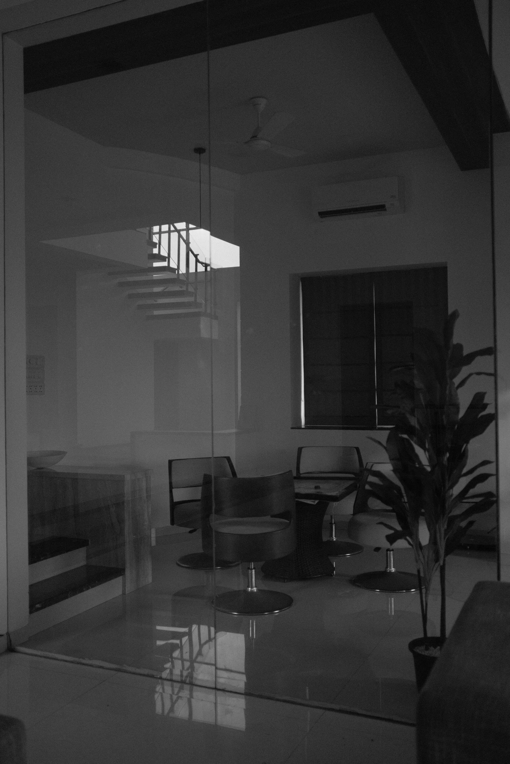 Une pièce à l'intérieur vue à travers une vitre, avec des chaises, une table, un meuble et une porte-fenêtre, le tout dans un style moderne.