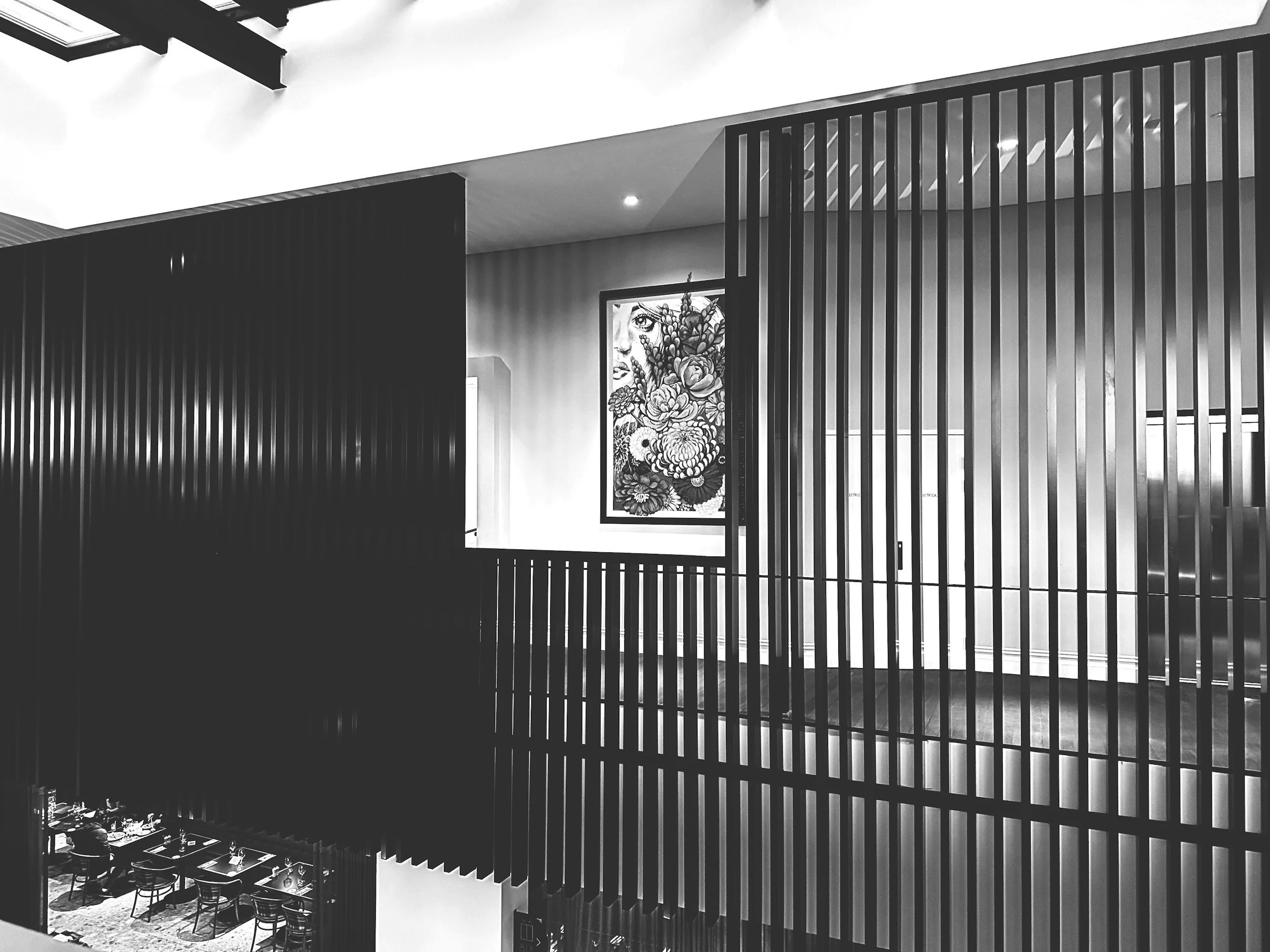Vue intérieure d'une salle de restaurant en hauteur, avec des tables et des chaises, un artwork de visage féminin avec des fleurs, divisée par des séparations en vertical, dans un style moderne et minimaliste.
