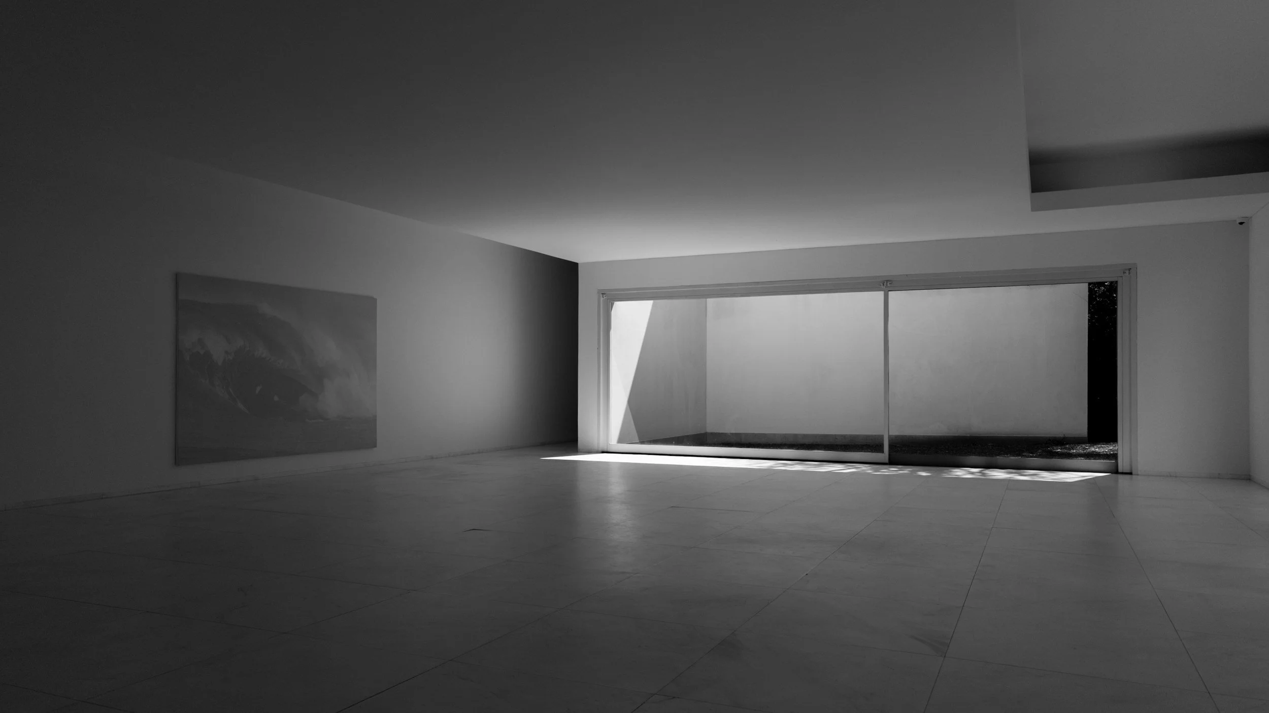 Salle d'exposition moderne avec mur blanc, artwork représentant une mer orageuse, et grande fenêtre laissant entrer la lumière naturelle.
