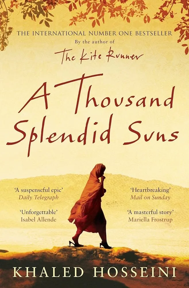 Book cover for 'A Thousand Splendid Suns' by Khaled Hosseini, featuring a woman in an orange dress walking across a desert landscape with a light yellow sky and autumn leaves at the top.