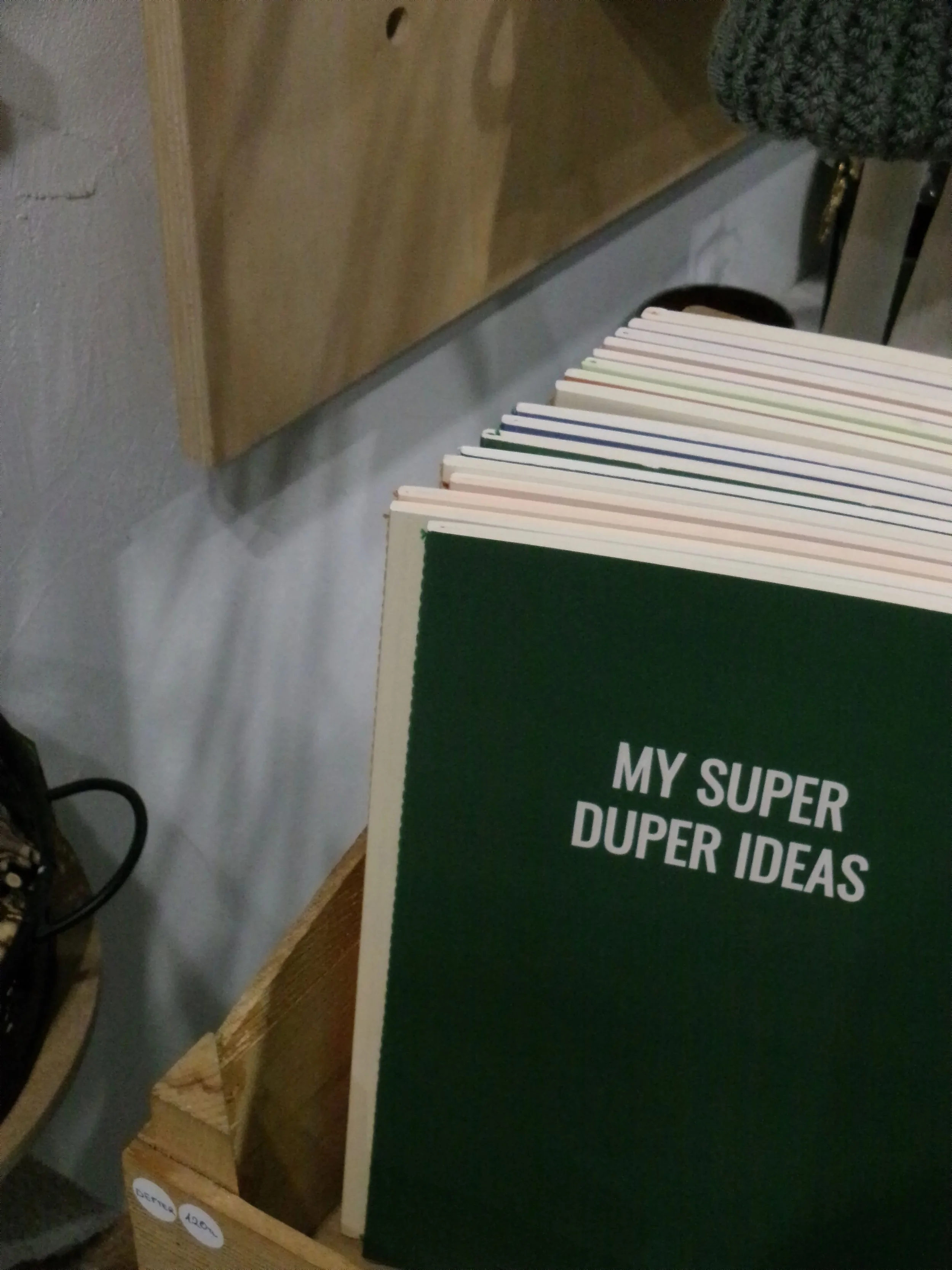 Close-up of a green book with white text reading "MY SUPER DUPER IDEAS" on the cover, placed on a desk.