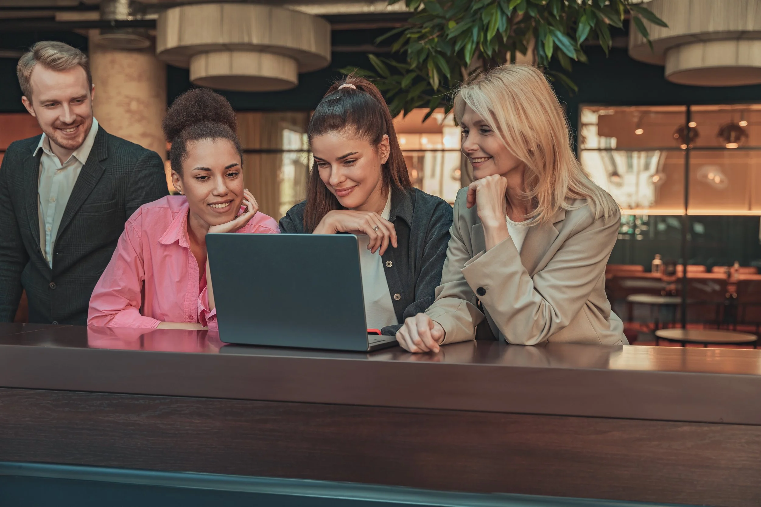 Business team collaborating on a laptop at a hotel bar, discussing hospitality marketing and business strategies.