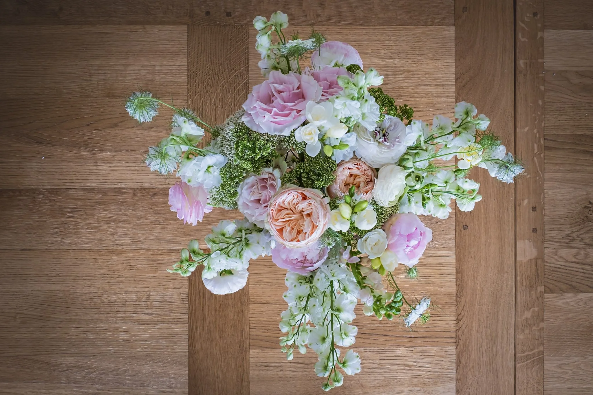 A bouquet of pink, white, and peach flowers with greenery, placed on a wooden surface.