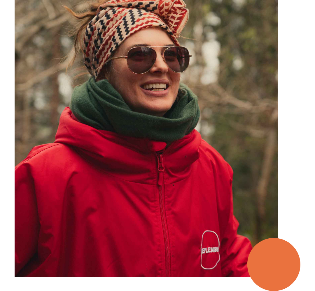 A woman wearing sunglasses, a patterned headscarf, a green scarf, and a red jacket outdoors.