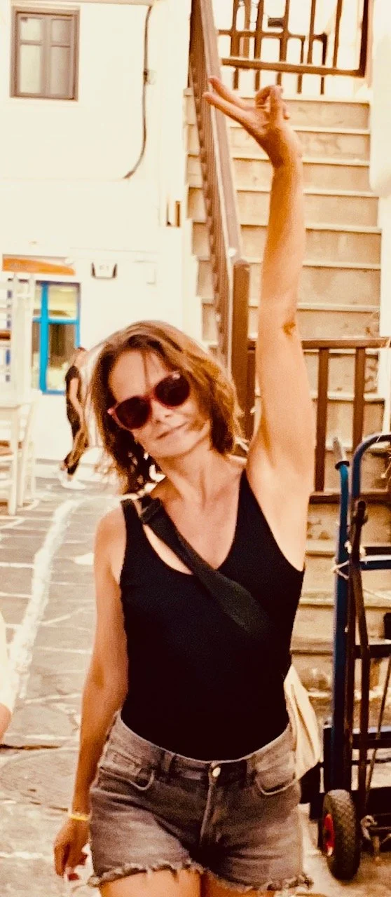 Frau mit Sonnenbrille und schwarzen Top, die auf einer Steiltreppe steht und die Arme in die Luft hebt.
