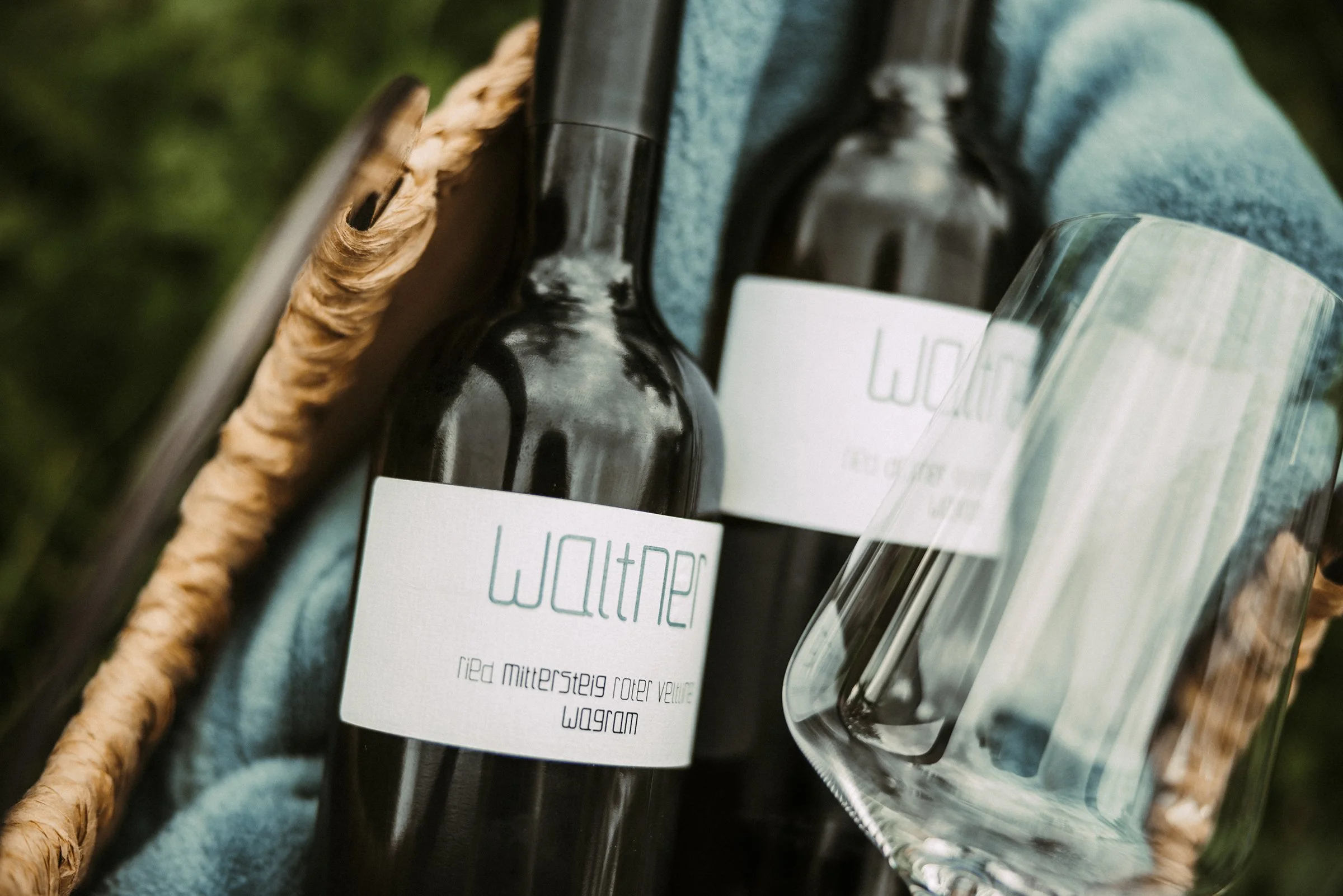 Nahaufnahme von Weinflaschen vom Weingut Waltner auf einem blauen, leichten Stoff in einem geflochtenen Korb.