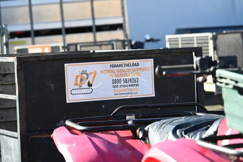 A black metal box with a sticker promoting mental health support in agriculture, placed outdoors on a farm or industrial area.