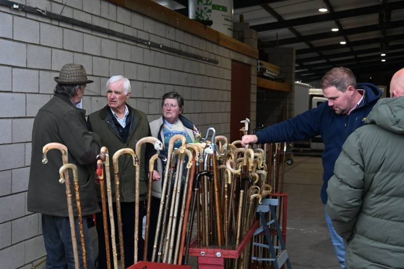 People examining antique umbrellas in a warehouse or storage area with concrete block walls.