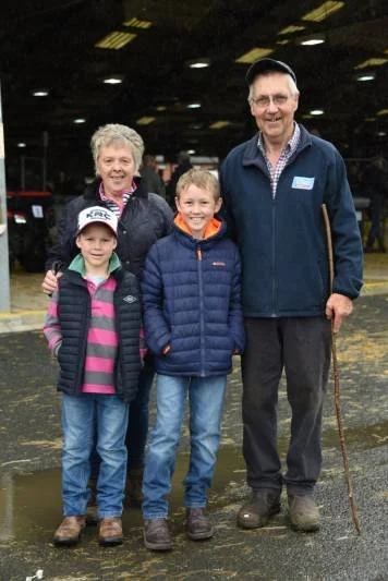 Family of four outdoors in an indoor or warehouse setting, smiling and posing for the camera, with a man holding a cane.