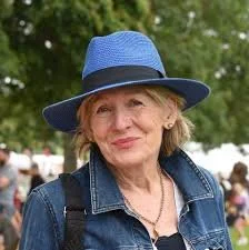 A woman wearing a blue hat and denim jacket outdoors at a public event.