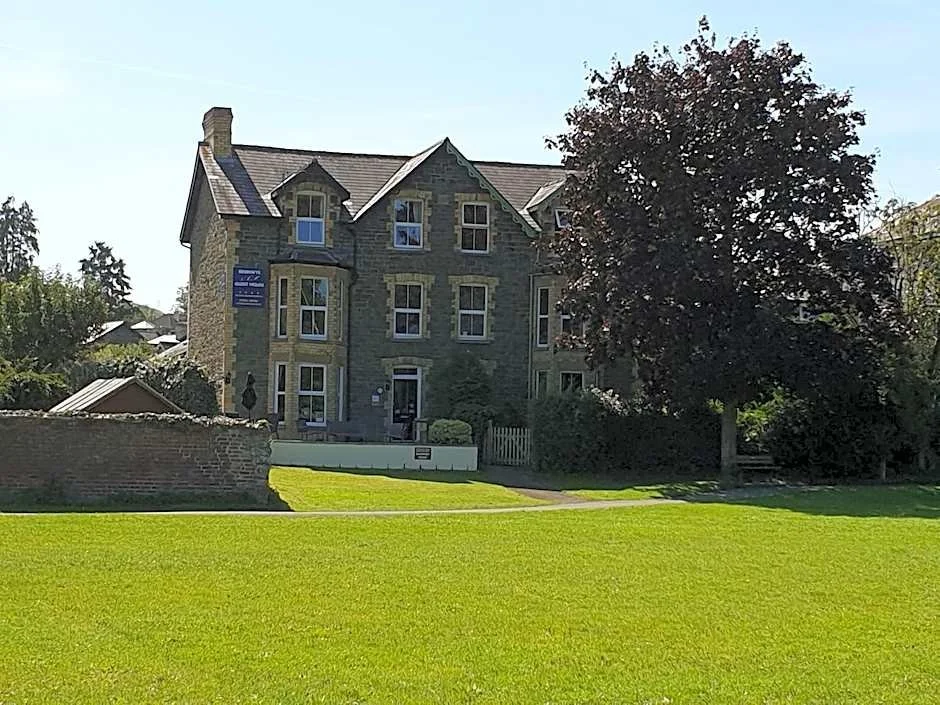 A large, historic stone building with multiple windows and a steep roof, surrounded by a well-maintained lawn and trees.
