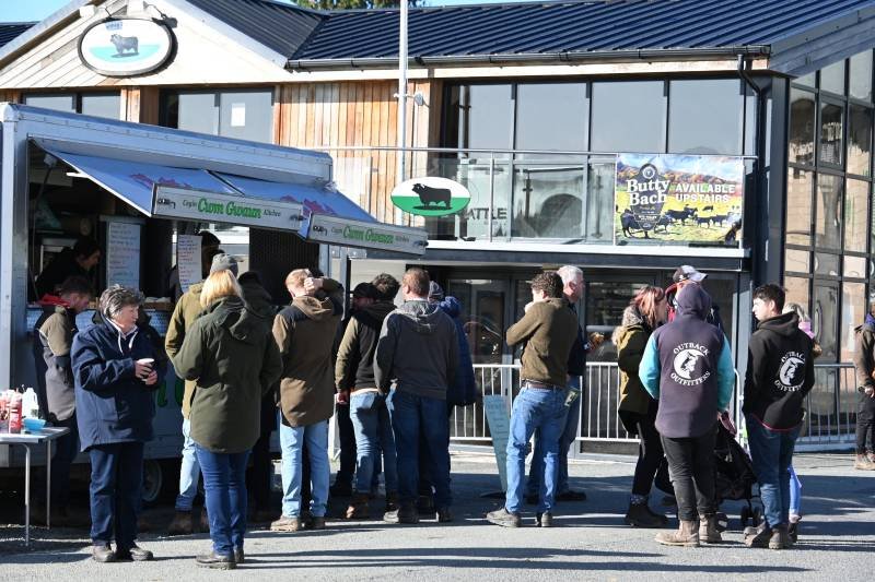 People lined up outside a grocery store with a sign indicating fresh seafood and an outdoor food stand.