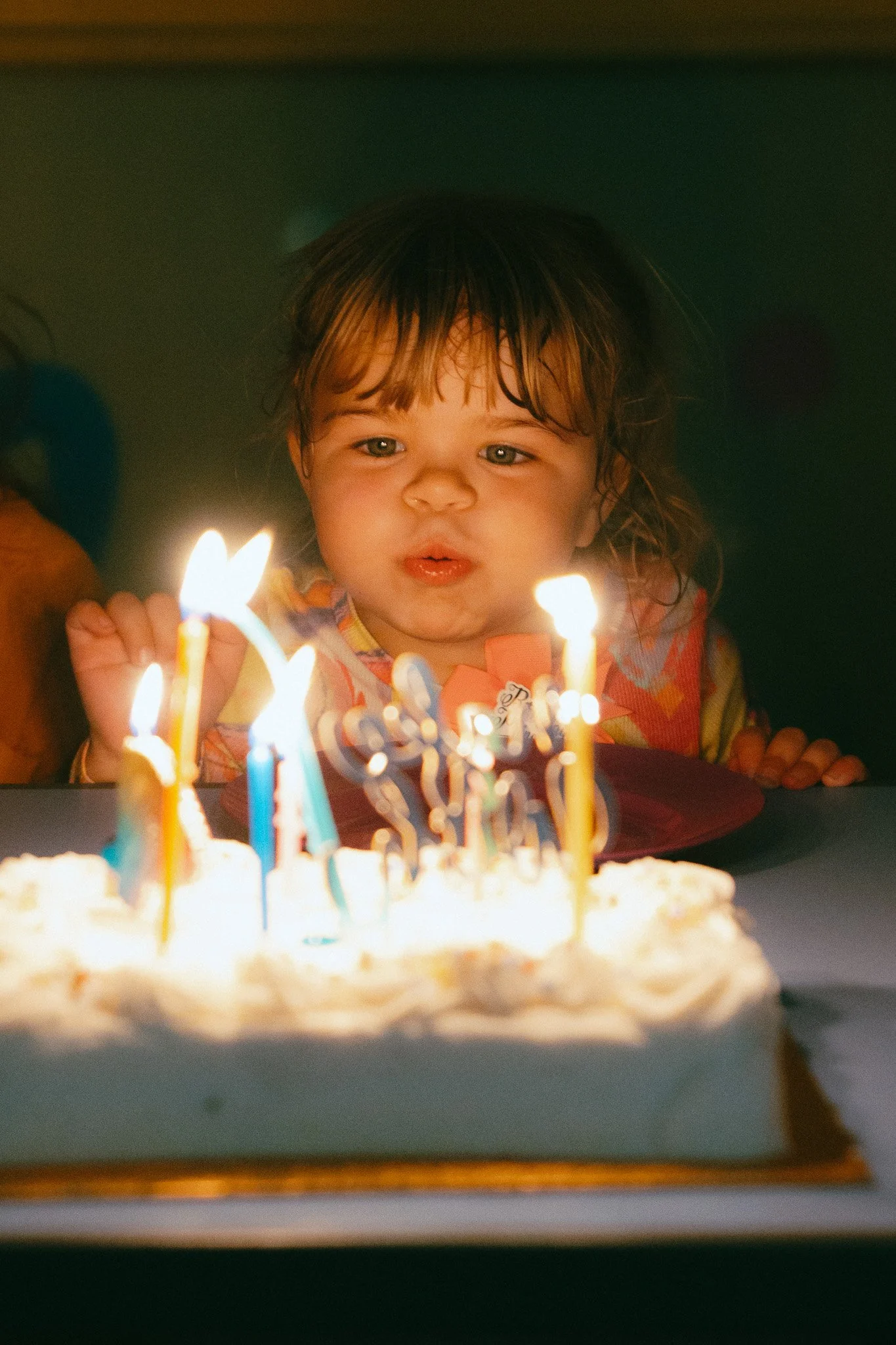 A young child with brown hair and big eyes blowing out birthday candles on a cake.