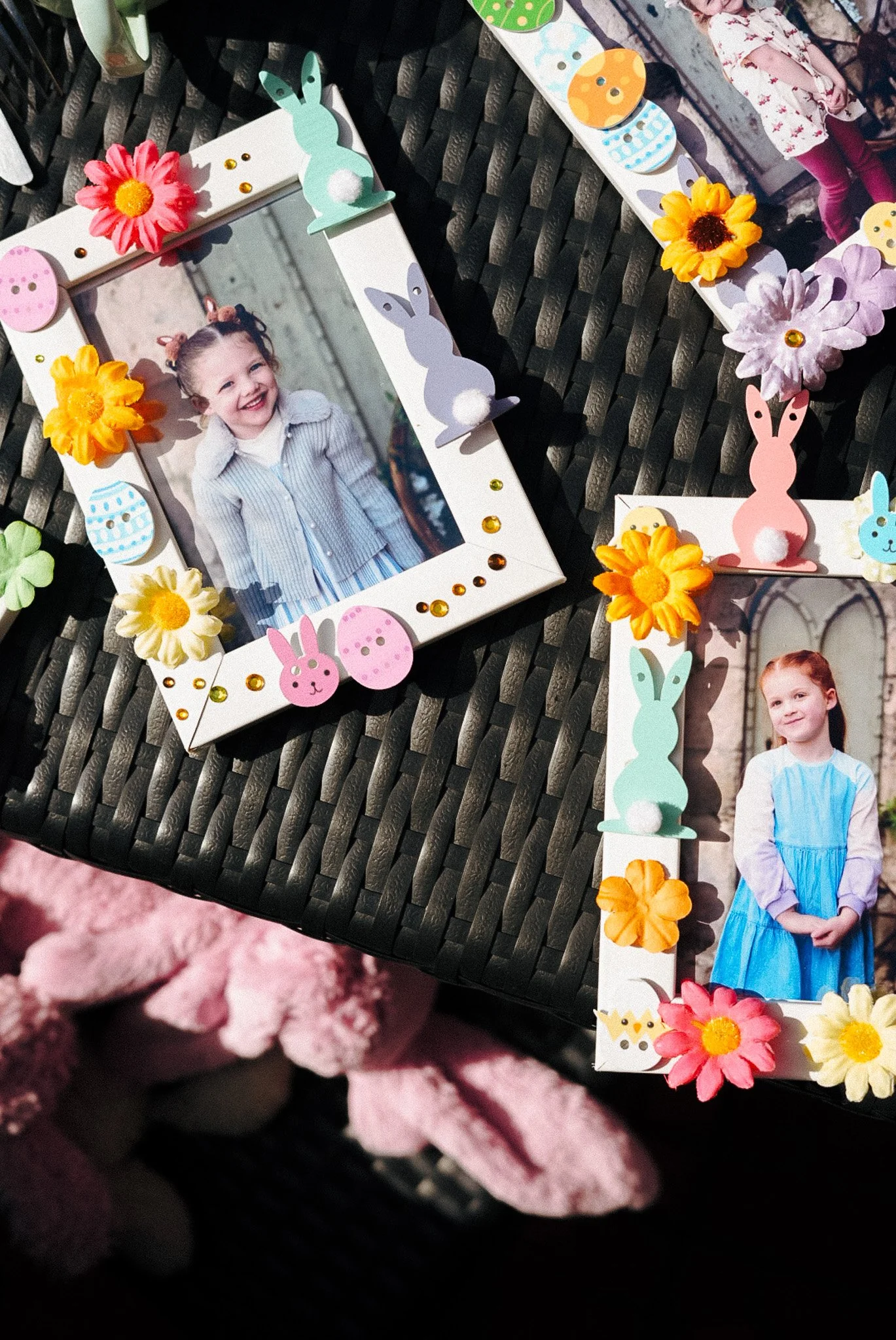 Decorative photo frames with children photos, surrounded by Easter-themed paper bunnies, flowers, and decorations on a black woven surface.