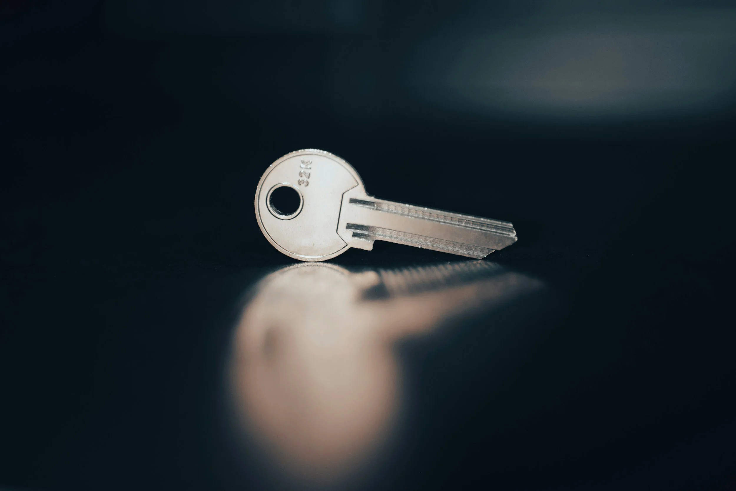 Close-up of a silver key lying on a dark surface with a soft reflection.